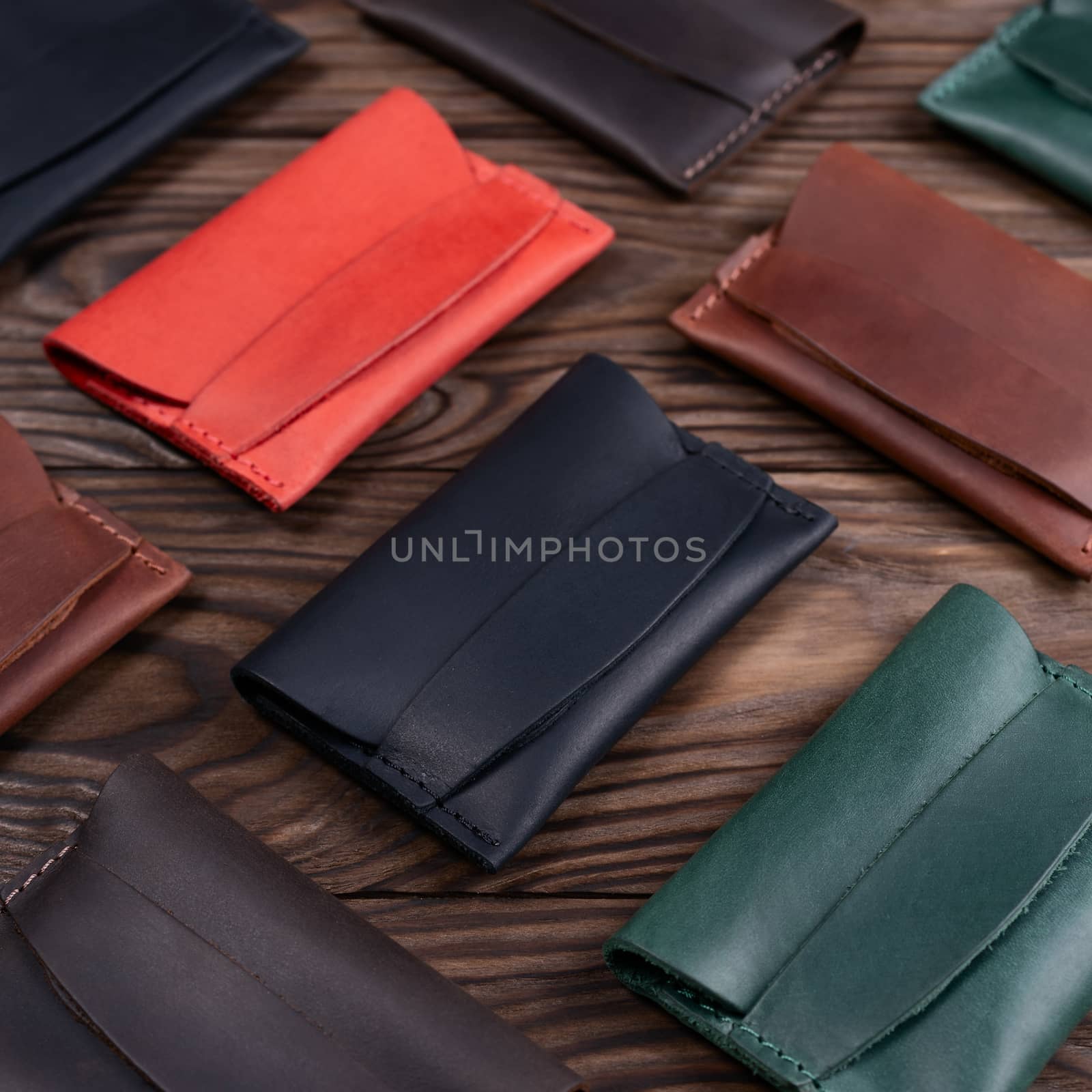 Flat lay photo of five different colour handmade leather one pocket cardholders.  Red, black, blown, ginger and green colors. Stock photo on wooden background.