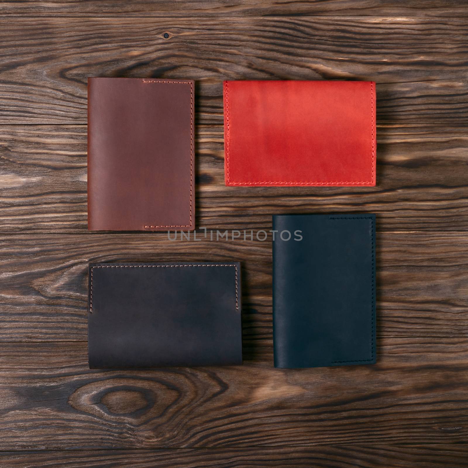 Four handmade leather passport covers on wooden textured background. Black, red, ginger and brown covers. Up to down view. Stock photo of luxury accessories.