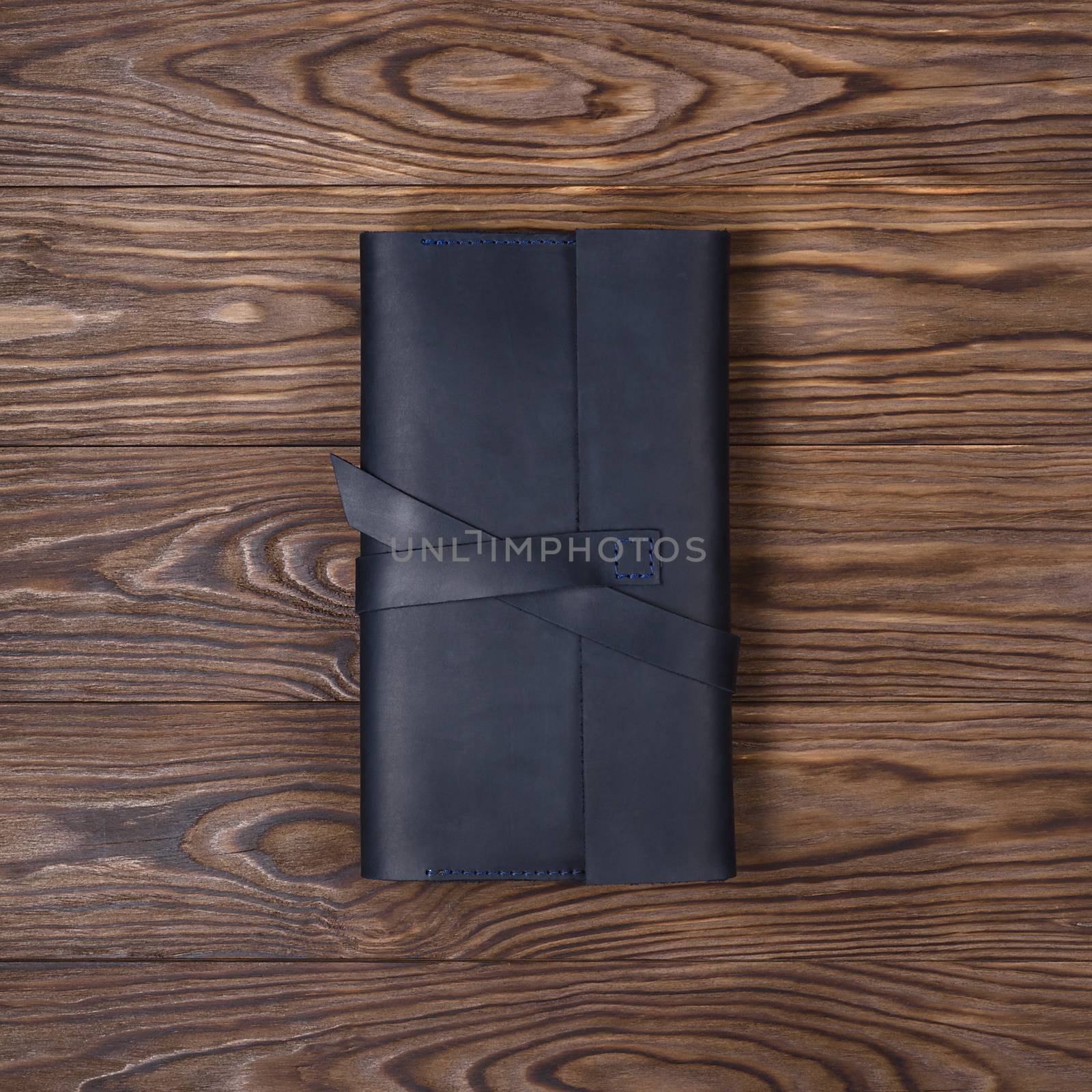 Black handmade travel wallet lies on textured wooden backgroud. Up to down view. Stock photo of businessman accessories.