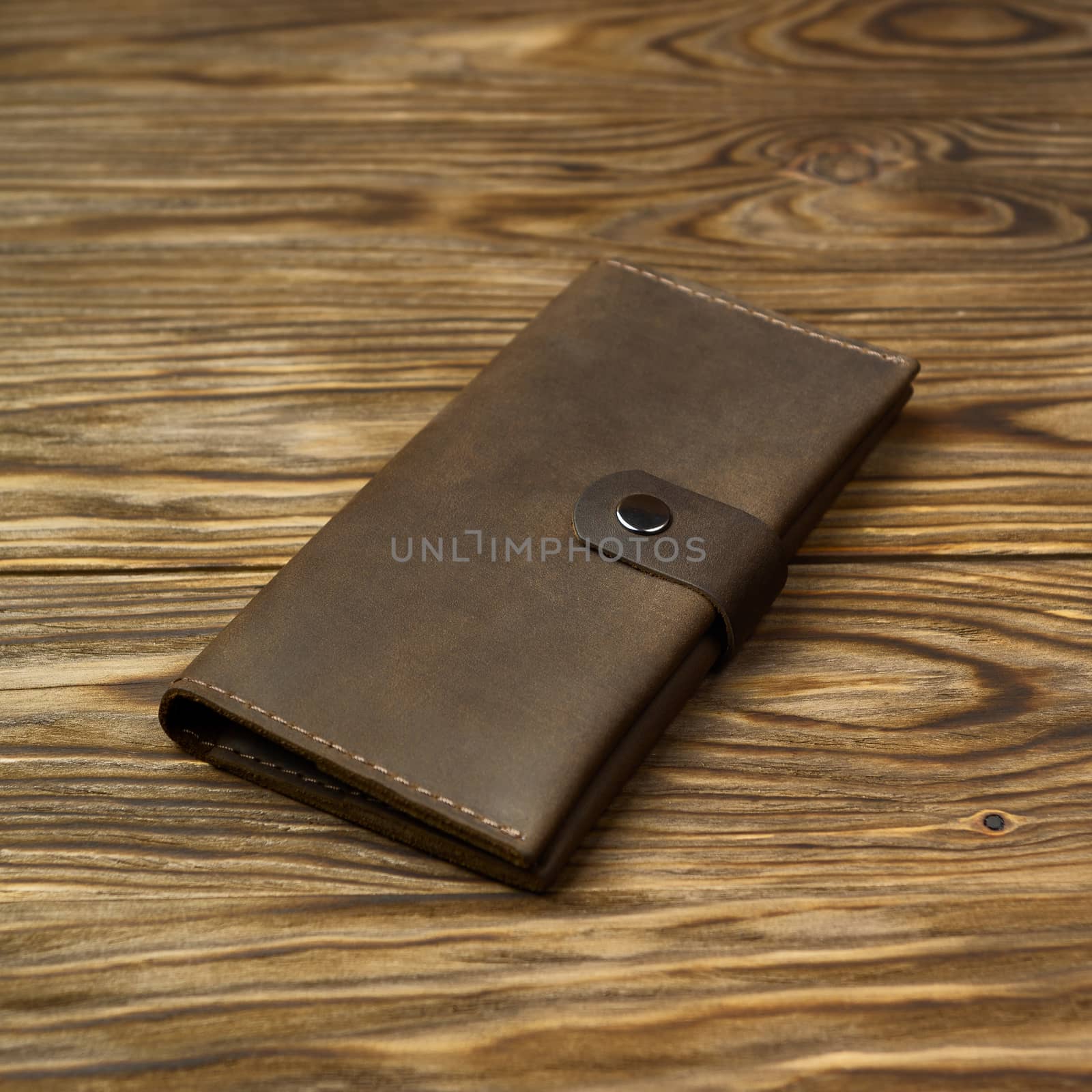 Brown color handmade leather wallet on textured wooden background. Wallet is unisex. Side view. Stock photo of luxury accessories.