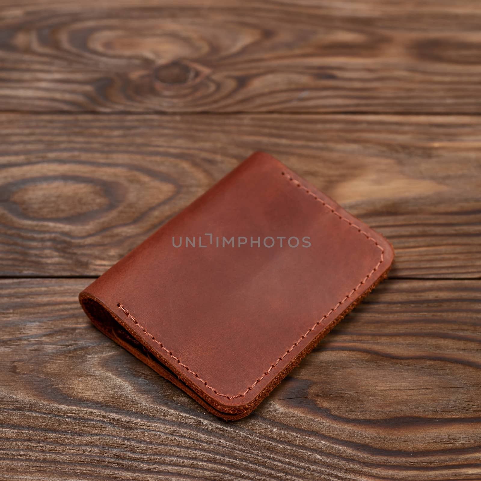 Ginger colour two-pocket closed leather handmade cardholder lies on wooden background. Soft focus on background. Stock photo on blurred background.