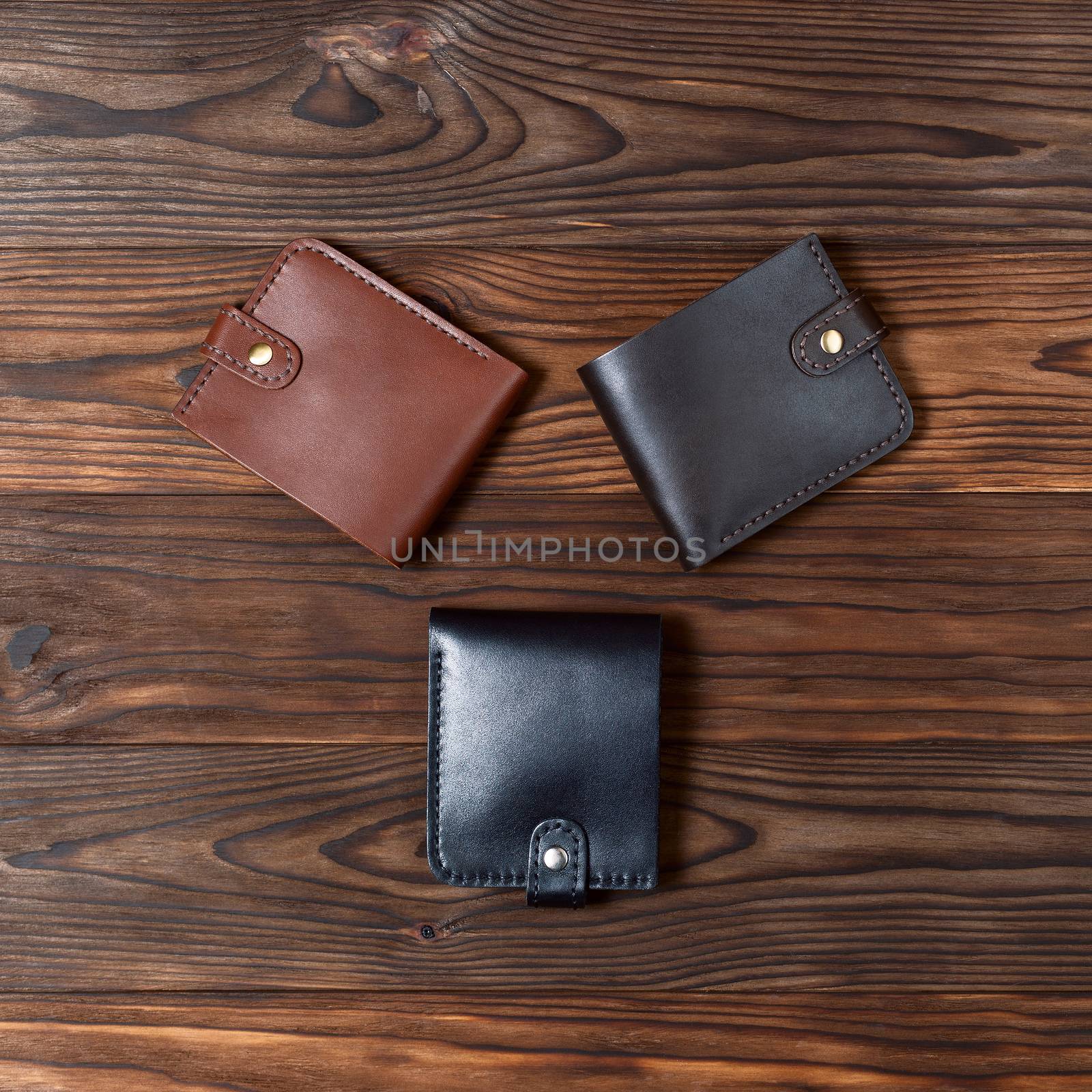Three handmade leather gloss wallets on wooden textured background. Up to down view. Businessman wallet stock photo. by alexsdriver