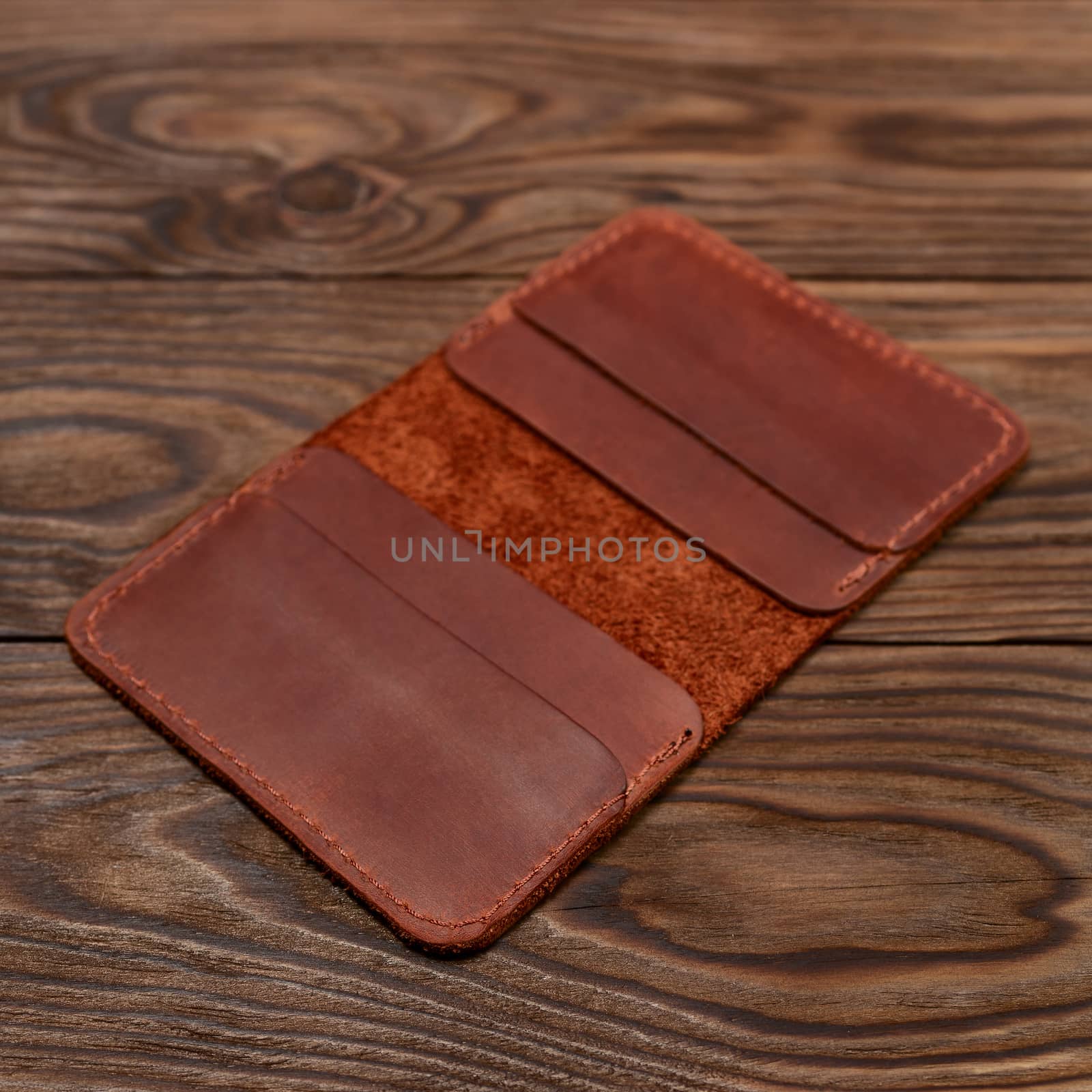 Handmade ginger colour leather cardholder on wooden background. Cardholder have 4 pockets for cards. Stock photo with soft focus background.