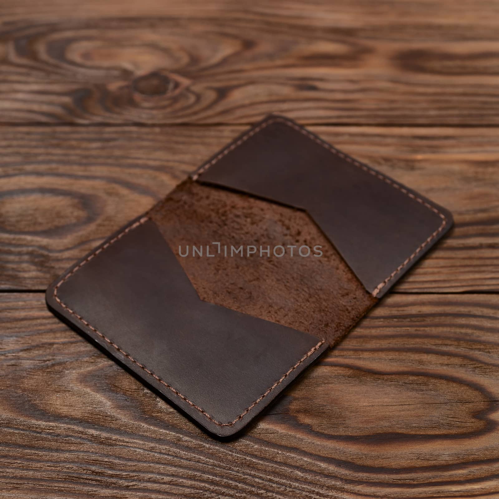 Handmade brown leather cardholder on wooden background. Stock photo with blurred background.