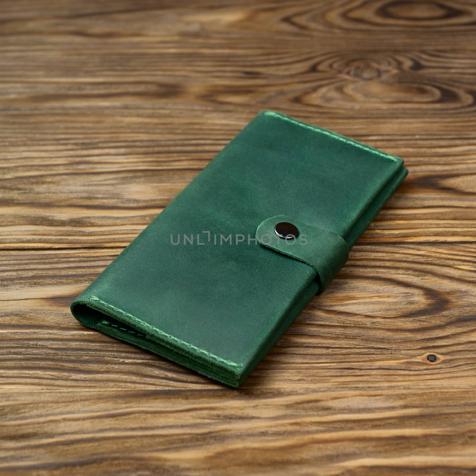 Green color handmade leather wallet on textured wooden background. Wallet is unisex. Side view. Stock photo of luxury accessories. by alexsdriver