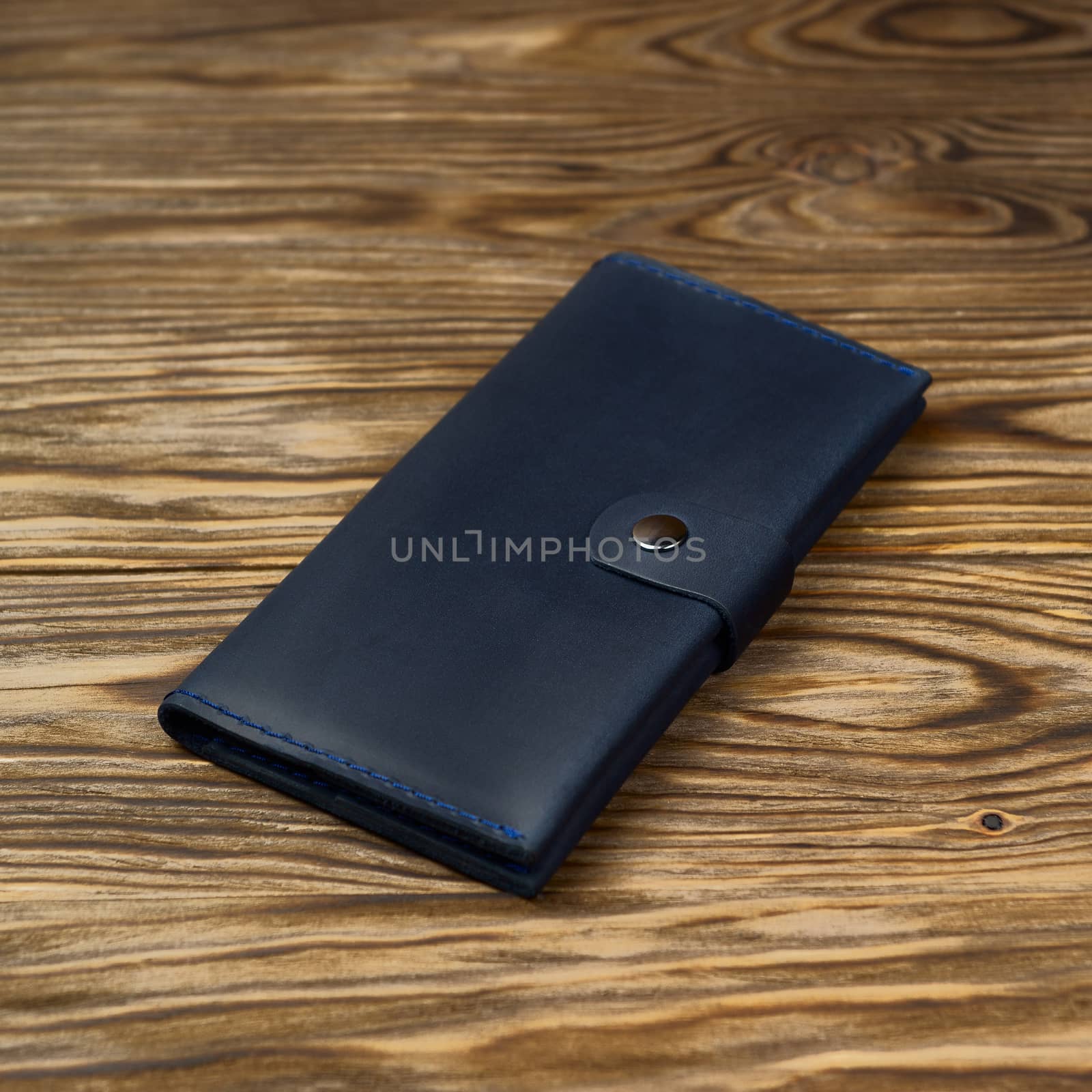Dark blue color handmade leather wallet on textured wooden background. Wallet is unisex. Side view. Stock photo of luxury accessories.