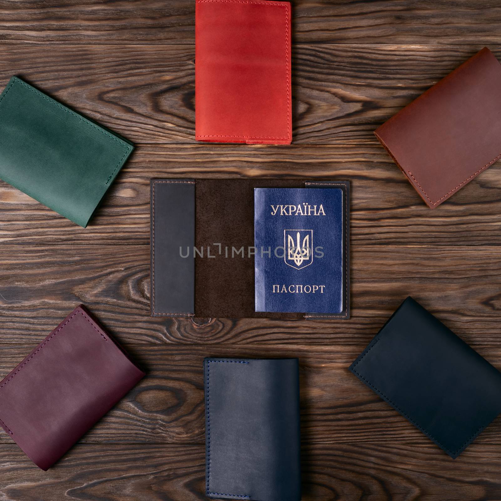 Six handmade leather passport covers around one opened cover on wooden textured background. Up to down view. Stock photo of luxury accessories.
