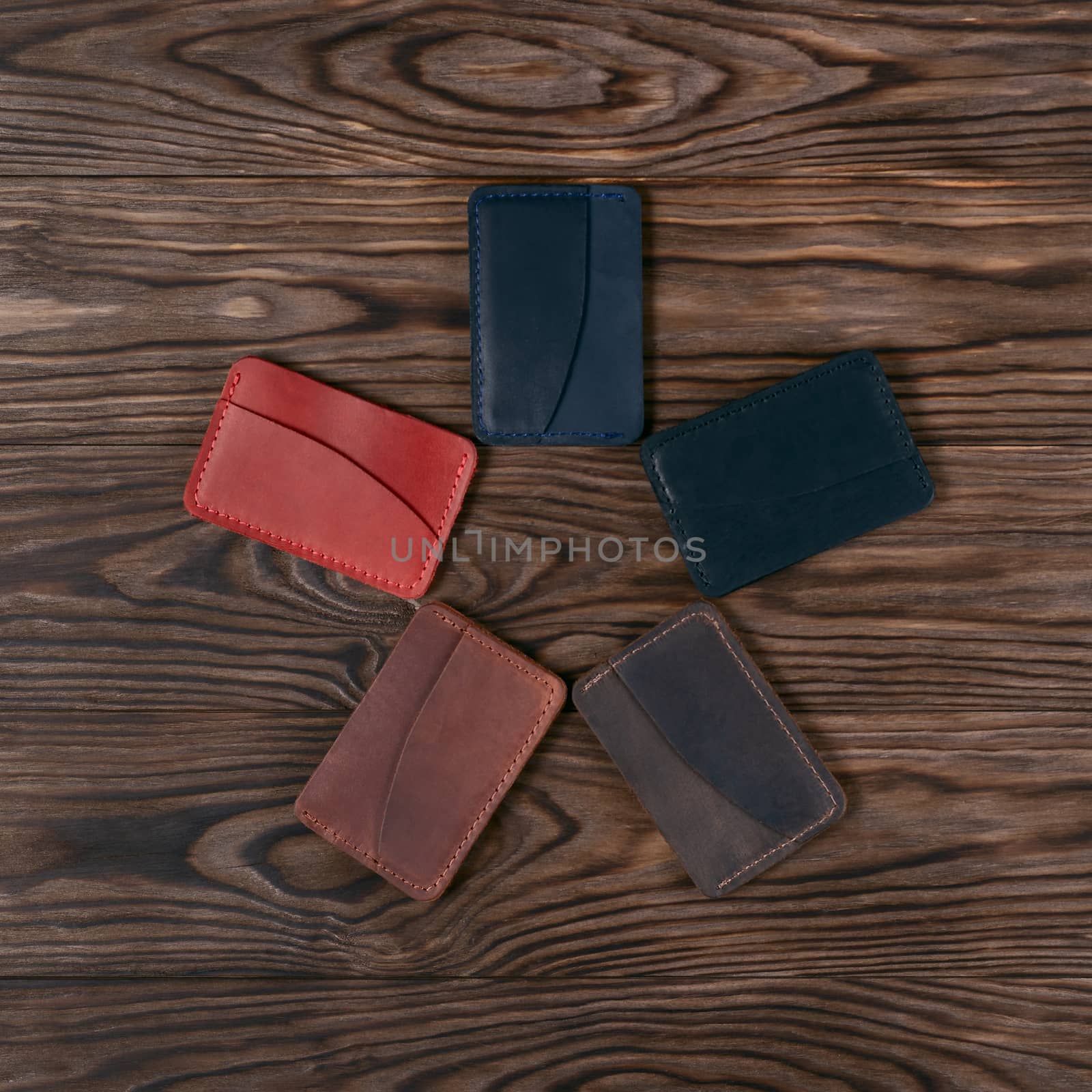 Five handmade leather cardholders on wooden background lies star shaped. Stock photo on perfect wooden background. Blue, black, brown, ginger and red items on photo. by alexsdriver