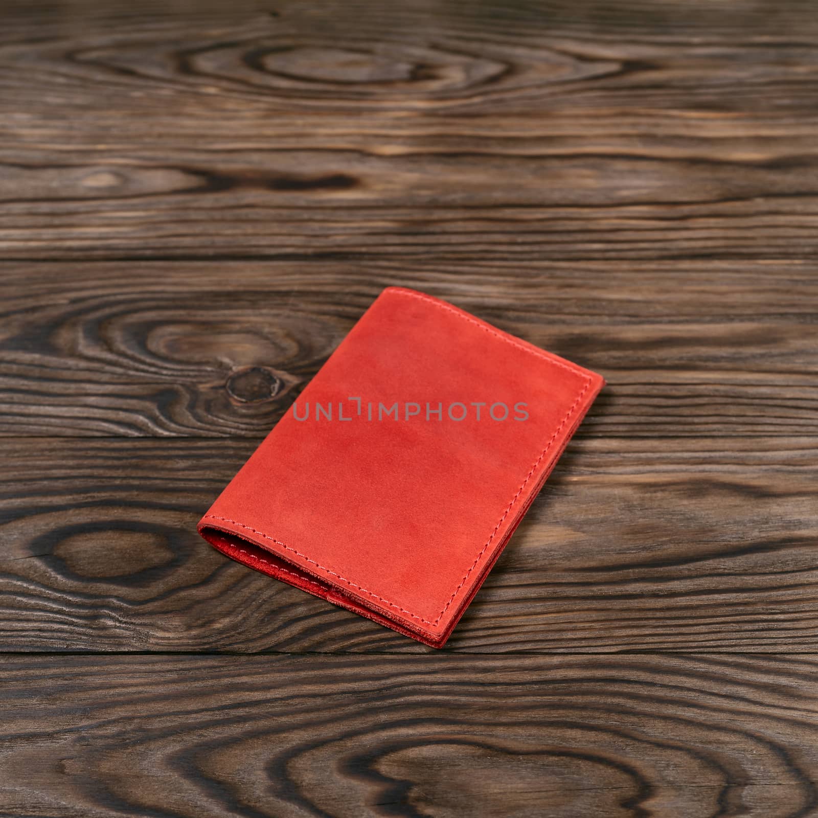 Red color handmade leather passport cover on wooden textured background. Businessman`s accessory.