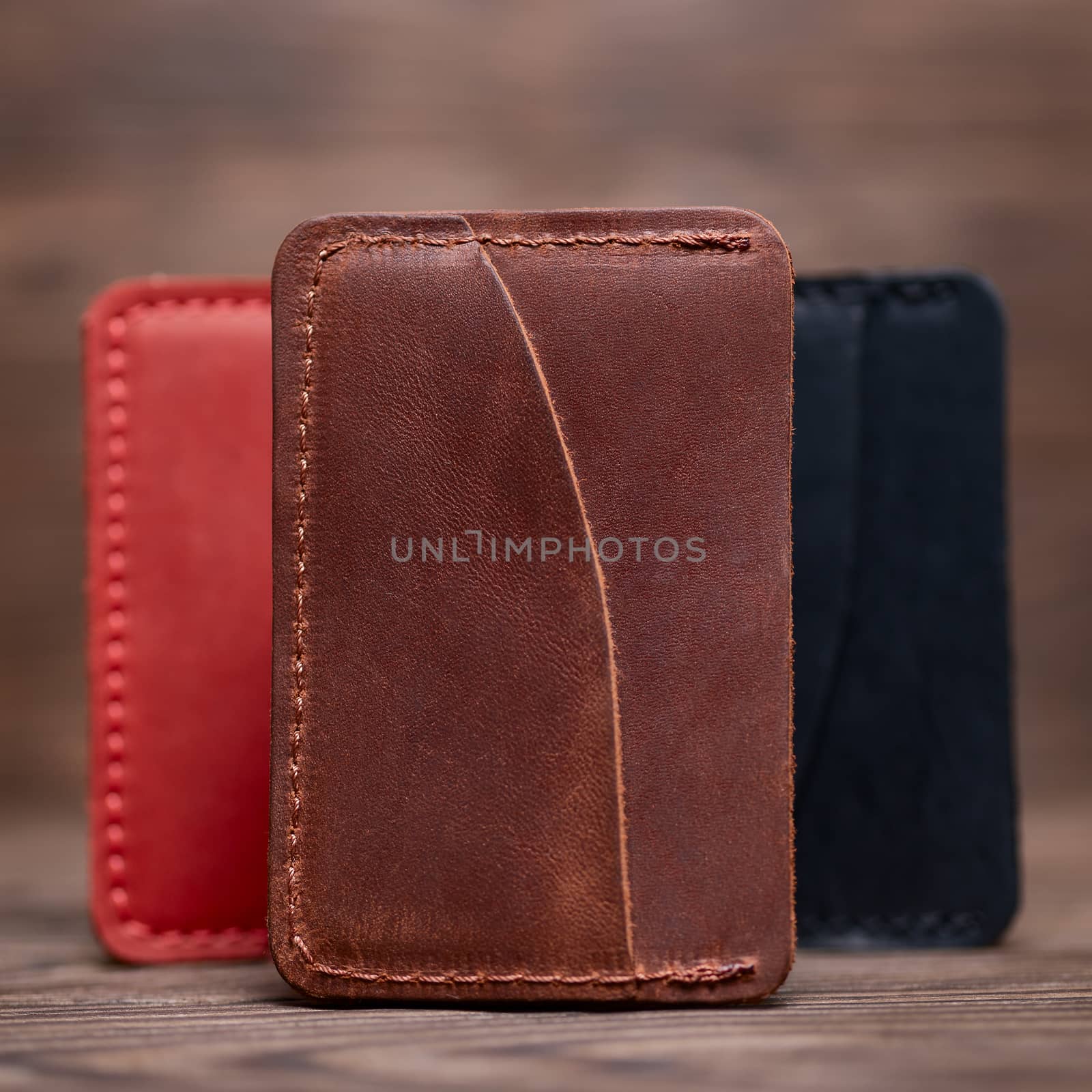 One pocket ginger colour leather handmade cardholder. On blurred background stay other colour cardholders. Stock photo on blurred background.