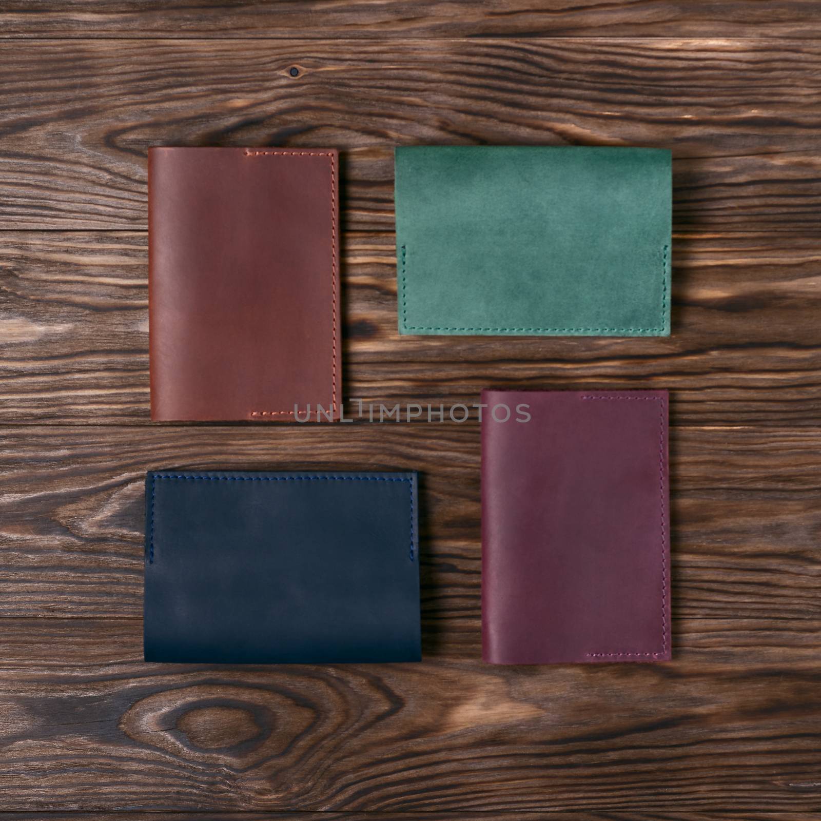 Four handmade leather passport covers on wooden textured background. Up to down view. Stock photo of luxury accessories.