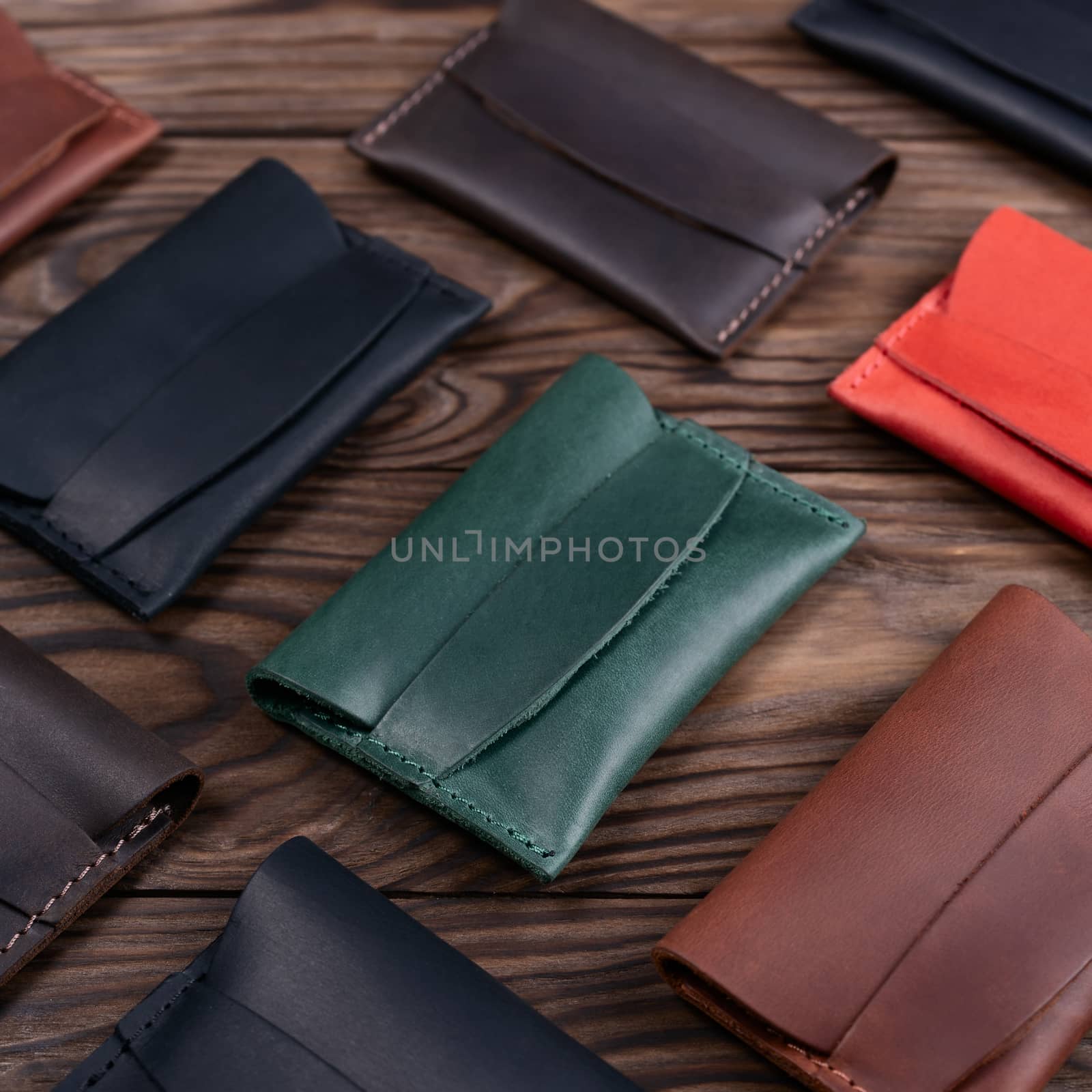 Flat lay photo of five different colour handmade leather one pocket cardholders.  Red, black, blown, ginger and green colors. Stock photo on wooden background.