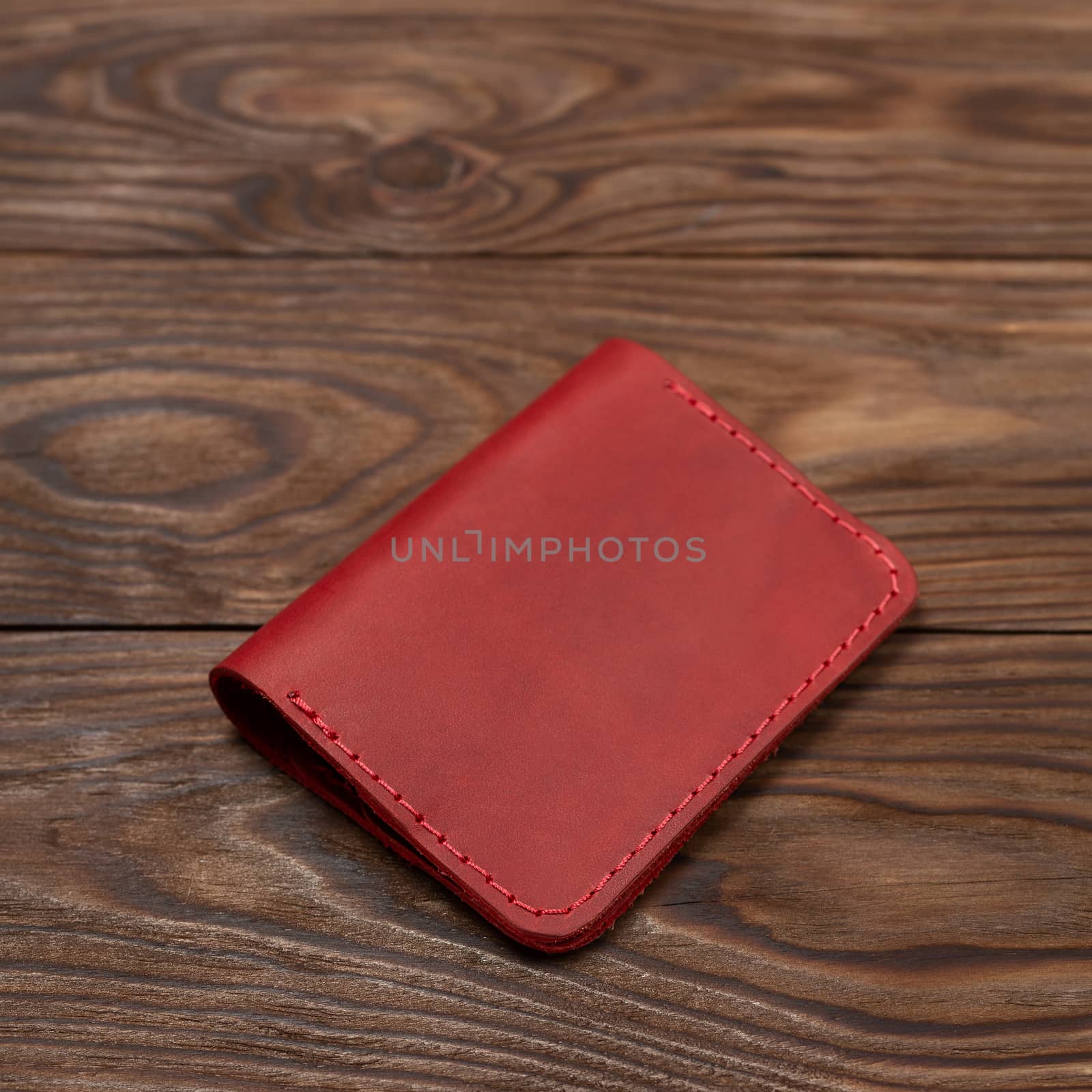 Red two-pocket closed leather handmade cardholder lies on wooden background. Soft focus on background. Stock photo on blurred background.