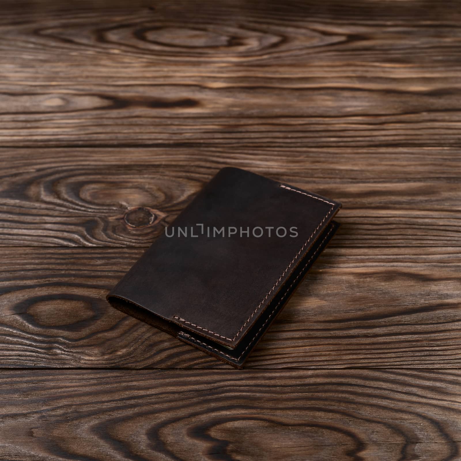 Brown color handmade leather passport cover on wooden textured background. Businessman`s accessory.