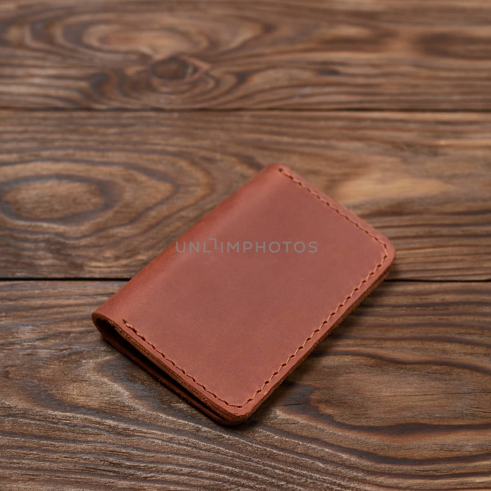 Ginger colour two-pocket closed leather handmade cardholder lies on wooden background. Soft focus on background. Stock photo on blurred background. by alexsdriver
