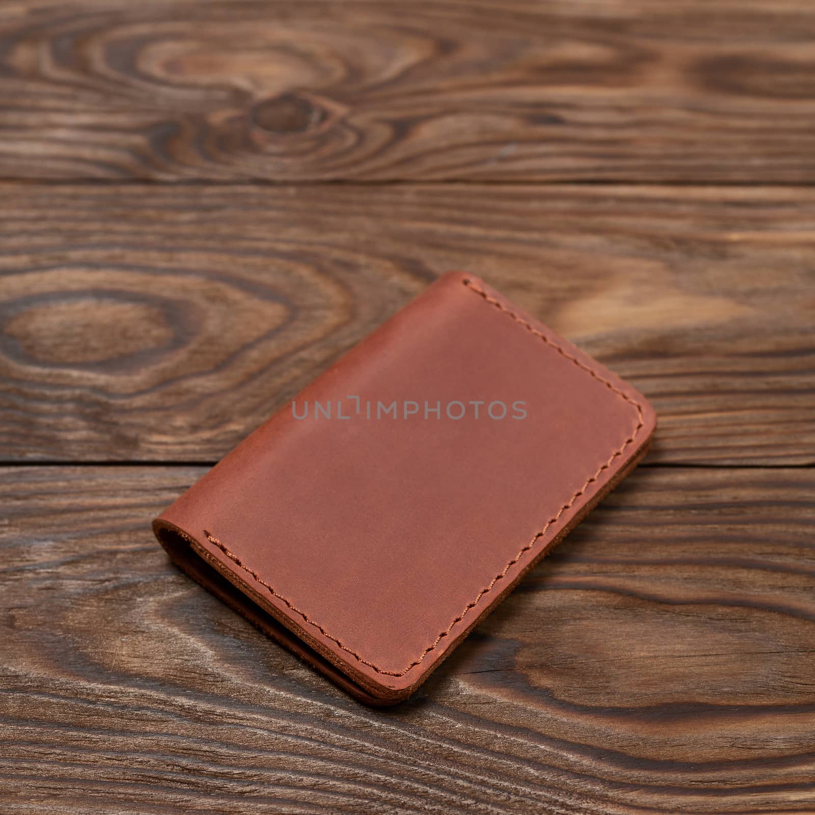 Ginger colour two-pocket closed leather handmade cardholder lies on wooden background. Soft focus on background. Stock photo on blurred background.