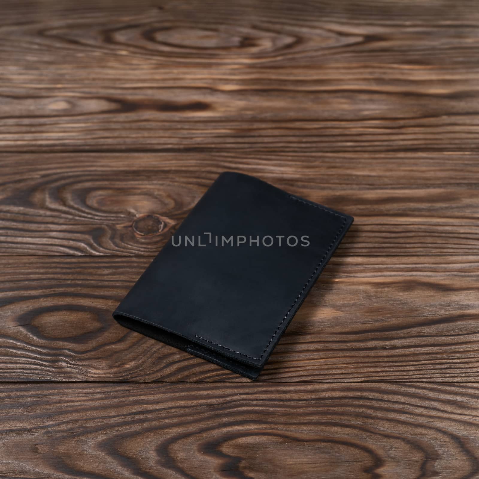 Black color handmade leather passport cover on wooden textured background. Businessman`s accessory.