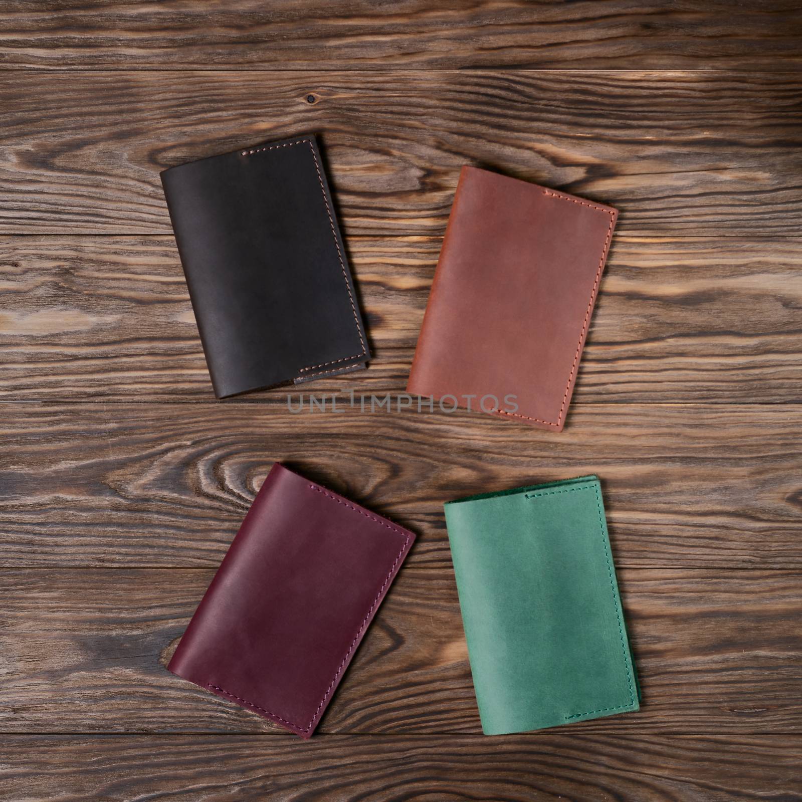 Four handmade leather passport covers on wooden textured background. Up to down view. Stock photo of luxury accessories.