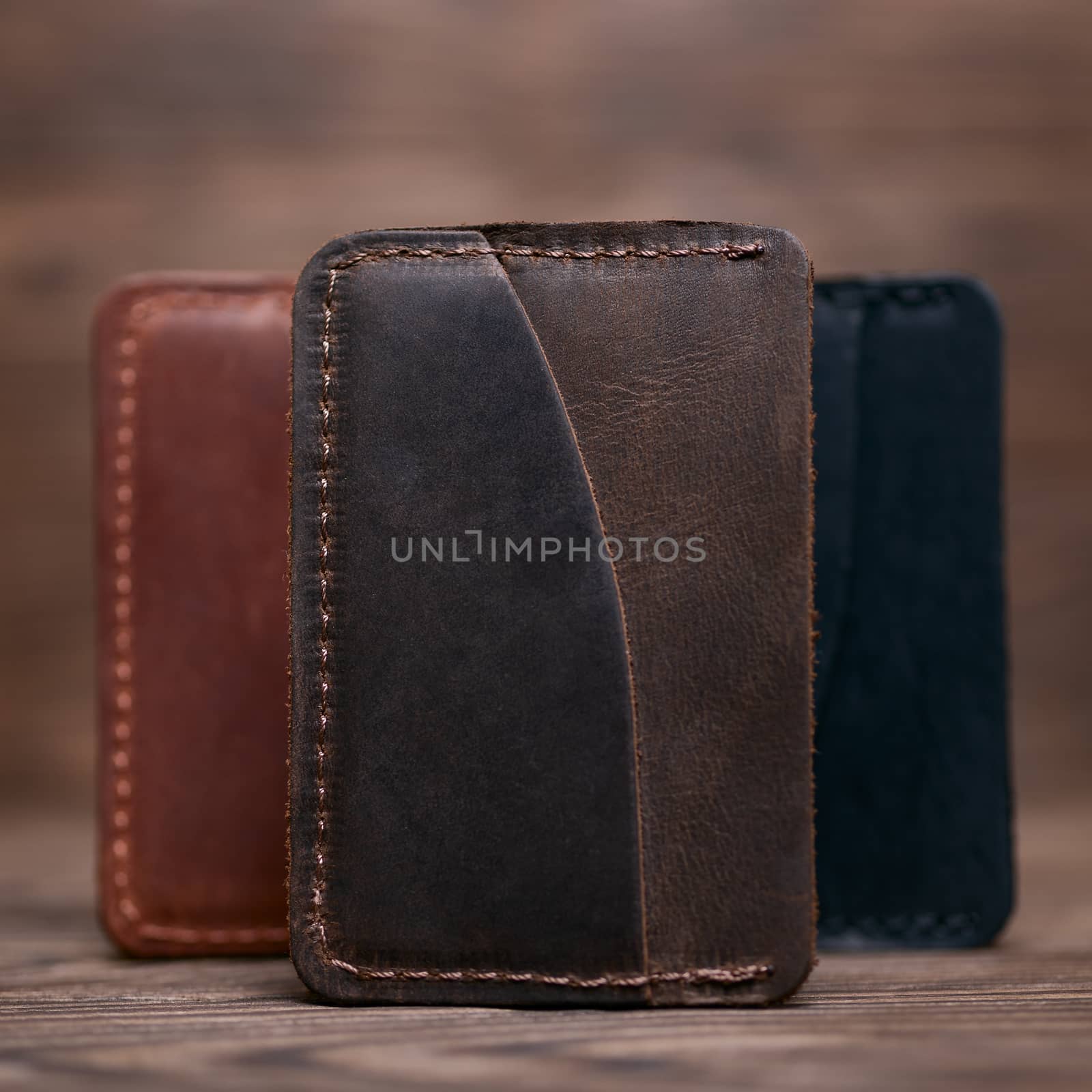 One pocket brown leather handmade cardholder. On blurred background stay other colour cardholders. Stock photo on blurred background. by alexsdriver
