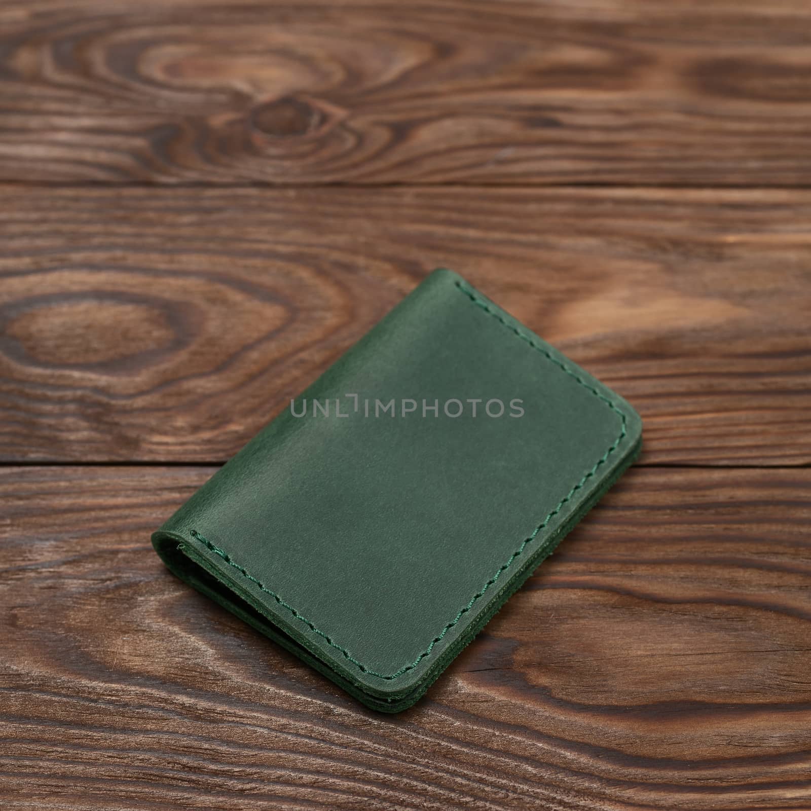 Green two-pocket closed leather handmade cardholder lies on wooden background. Soft focus on background. Stock photo on blurred background.