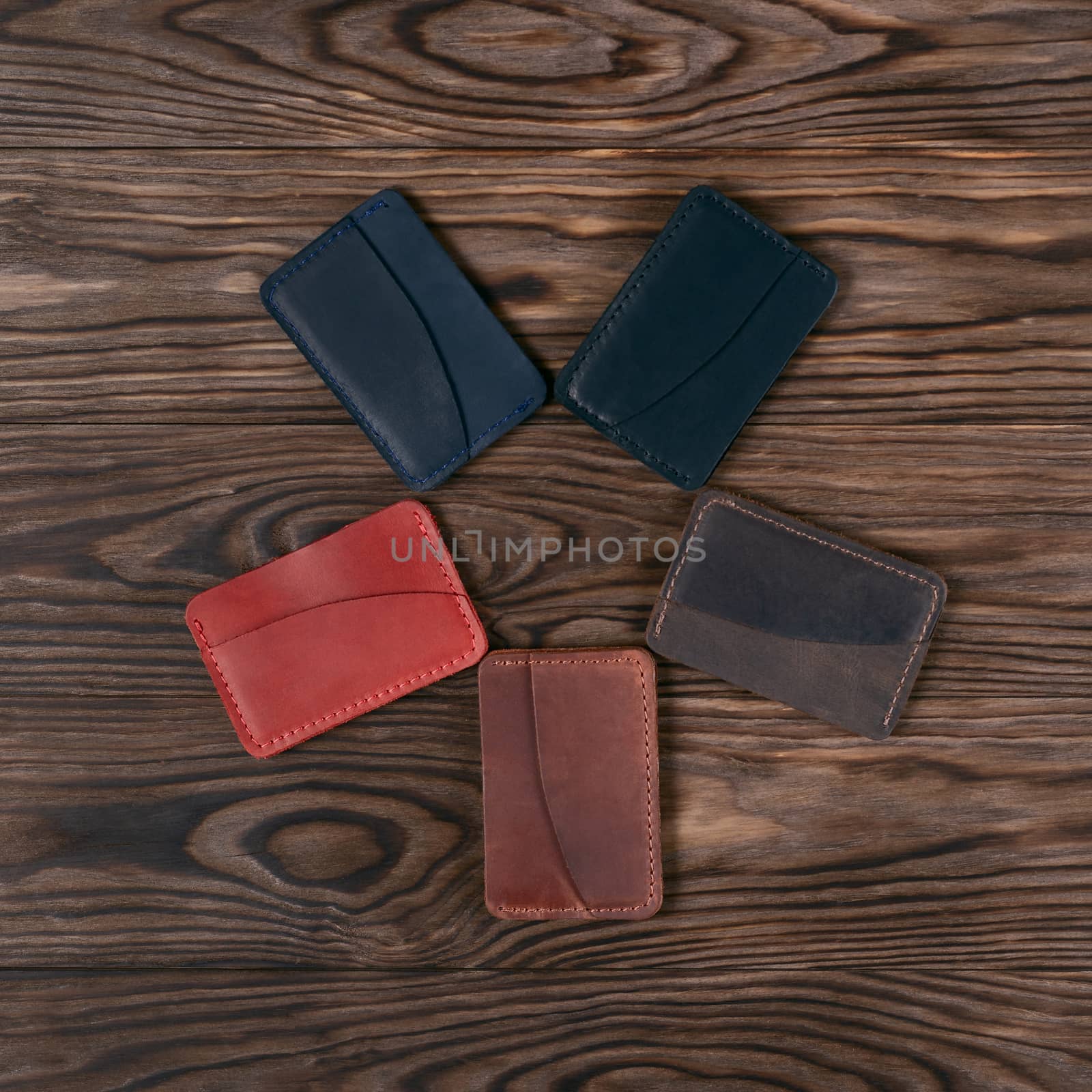 Five handmade leather cardholders on wooden background lie star shaped. Stock photo on perfect wooden background. Blue, black, brown, ginger and red items on photo.