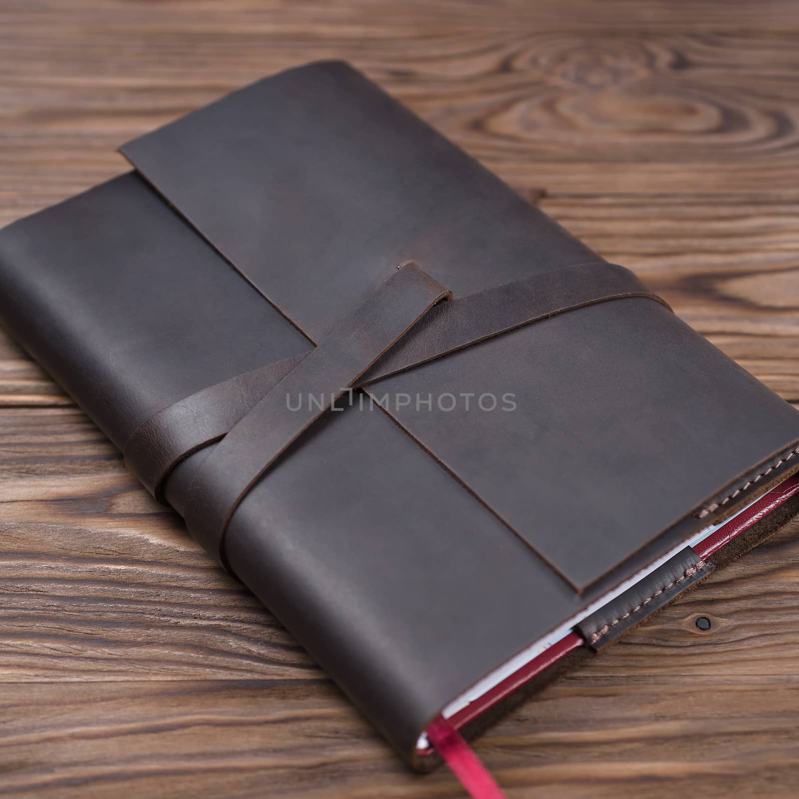 Brown handmade leather notebook cover with notebook inside on wooden background. Stock photo of luxury business accessories.