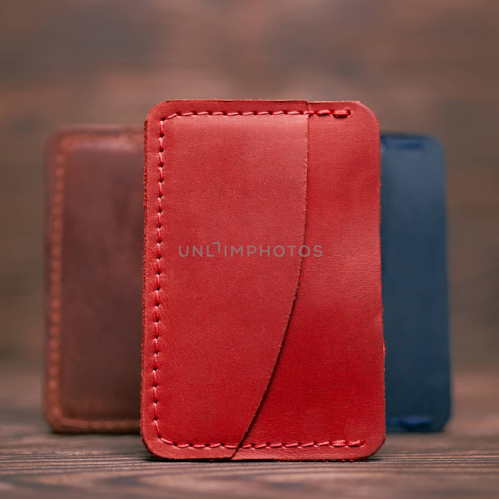One pocket red leather handmade cardholder. On blurred background stay other colour cardholders. Stock photo on blurred background. by alexsdriver