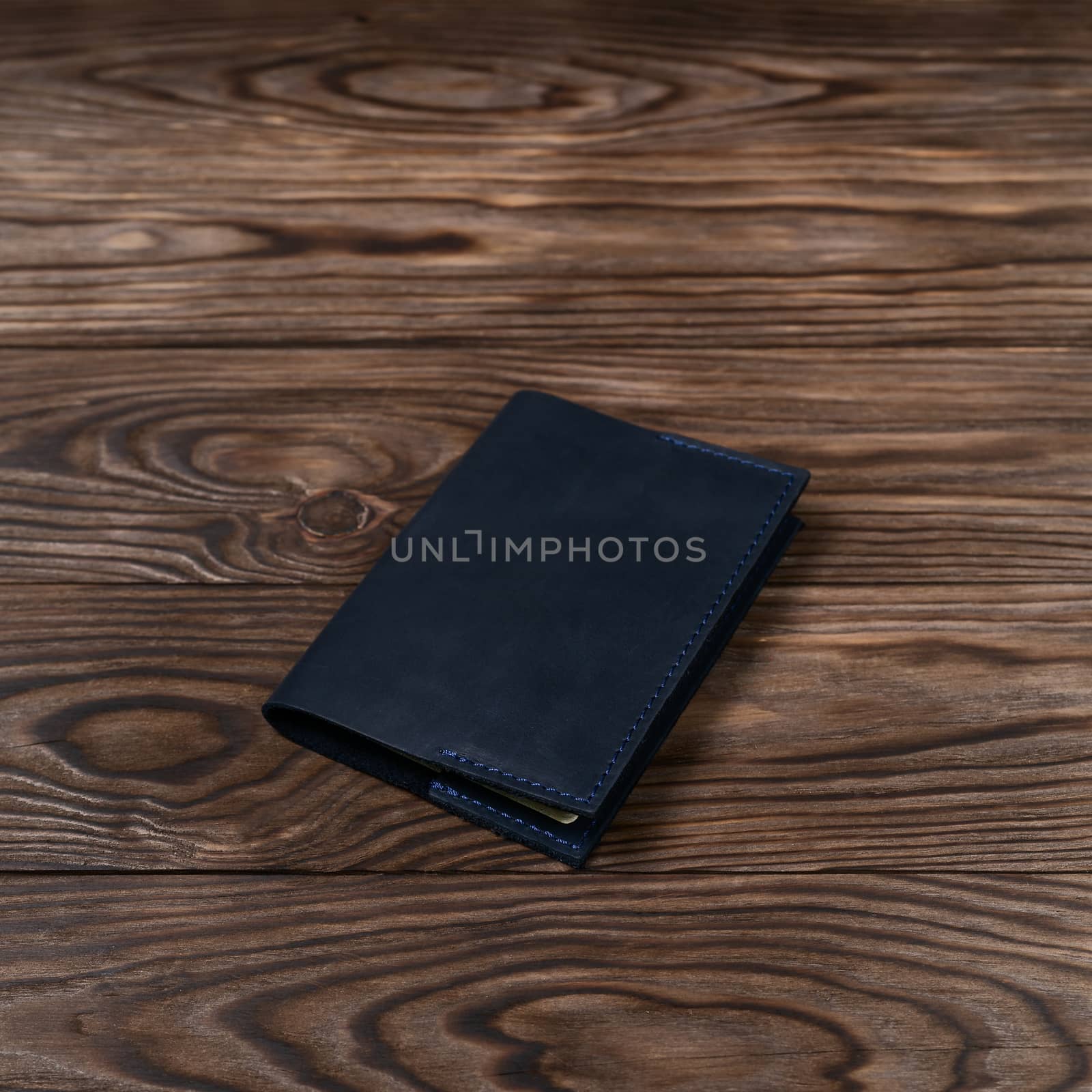 Blue color handmade leather passport cover on wooden textured background. Businessman`s accessory.