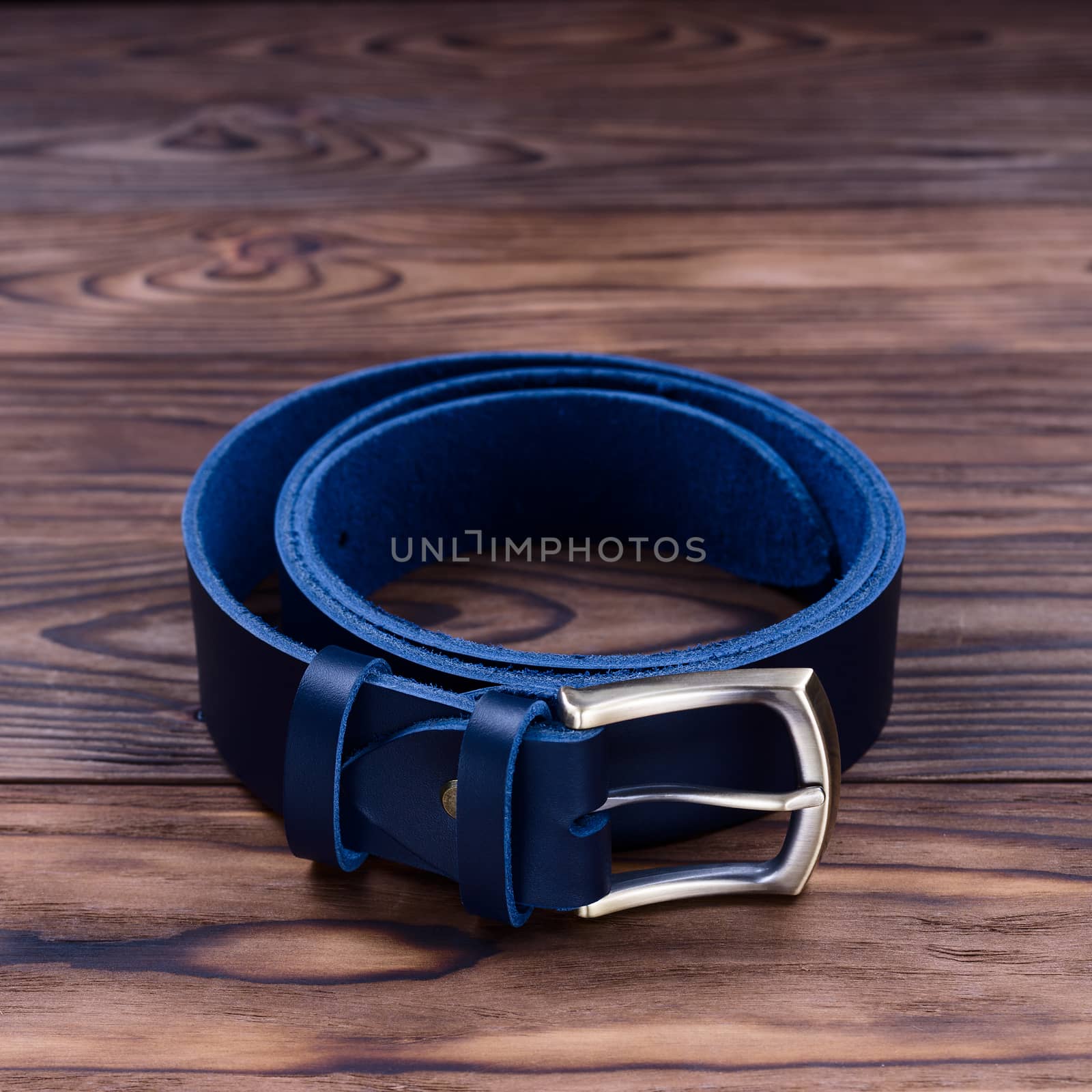 Blue color handmade belt lies on textured wooden background. The belt is twisted into a ring. Closeup side view. Stock photo of businessman accessories.