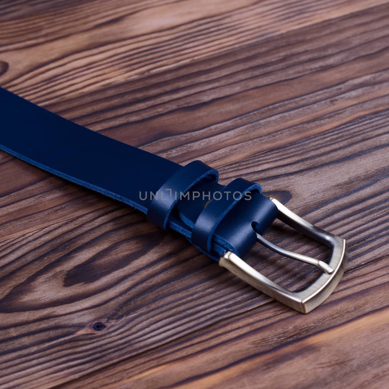 Hue blue handmade belt buckle lies on textured wooden background closeup. Side view. Stock photo of businessman accessories. by alexsdriver