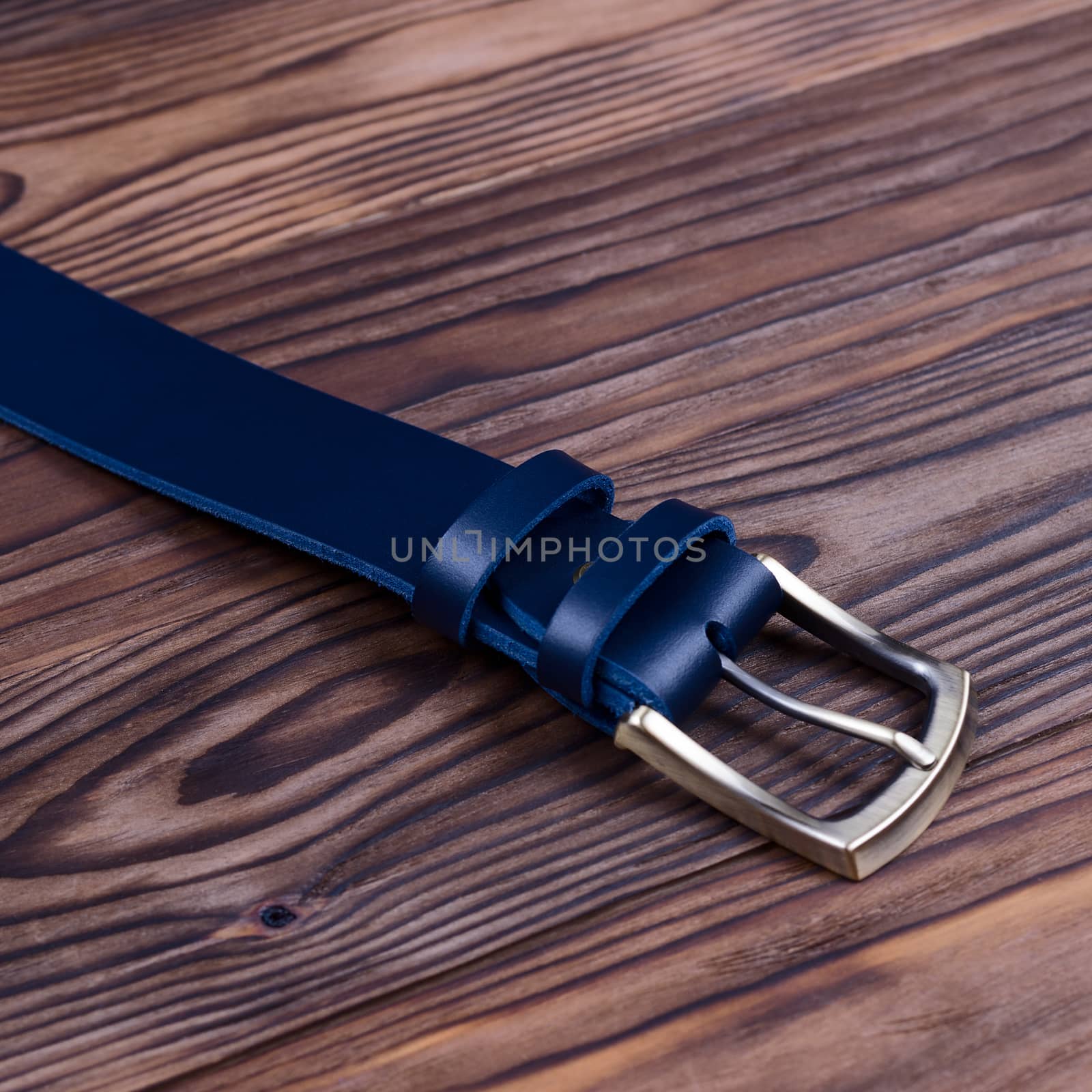 Hue blue handmade belt buckle lies on textured wooden background closeup. Side view. Stock photo of businessman accessories.