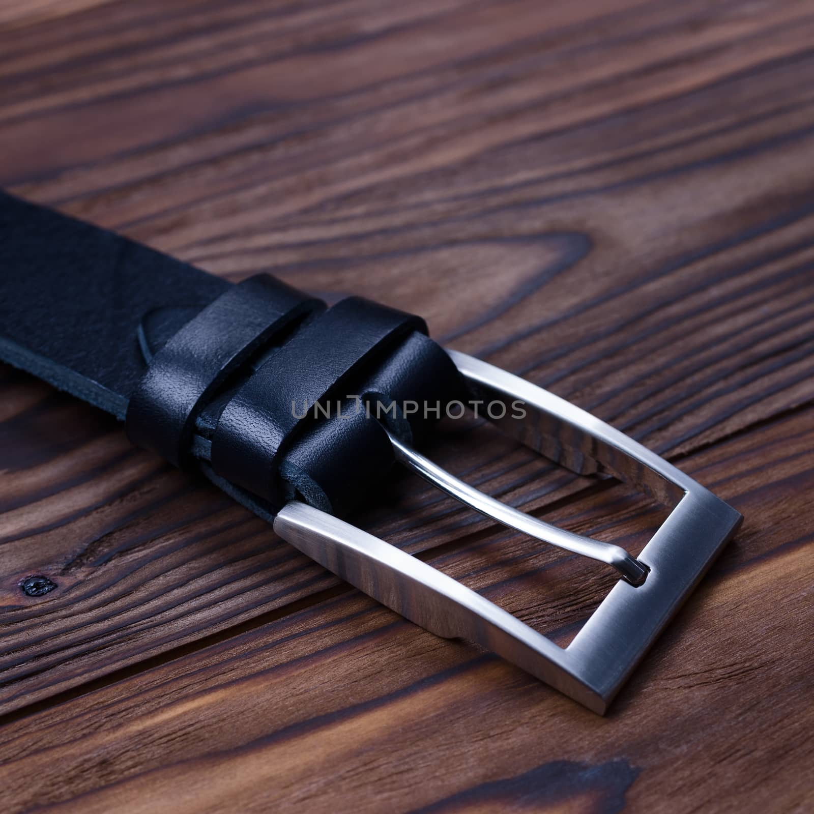 Black handmade belt buckle lies on textured wooden background closeup. Side view. Stock photo of businessman accessories.