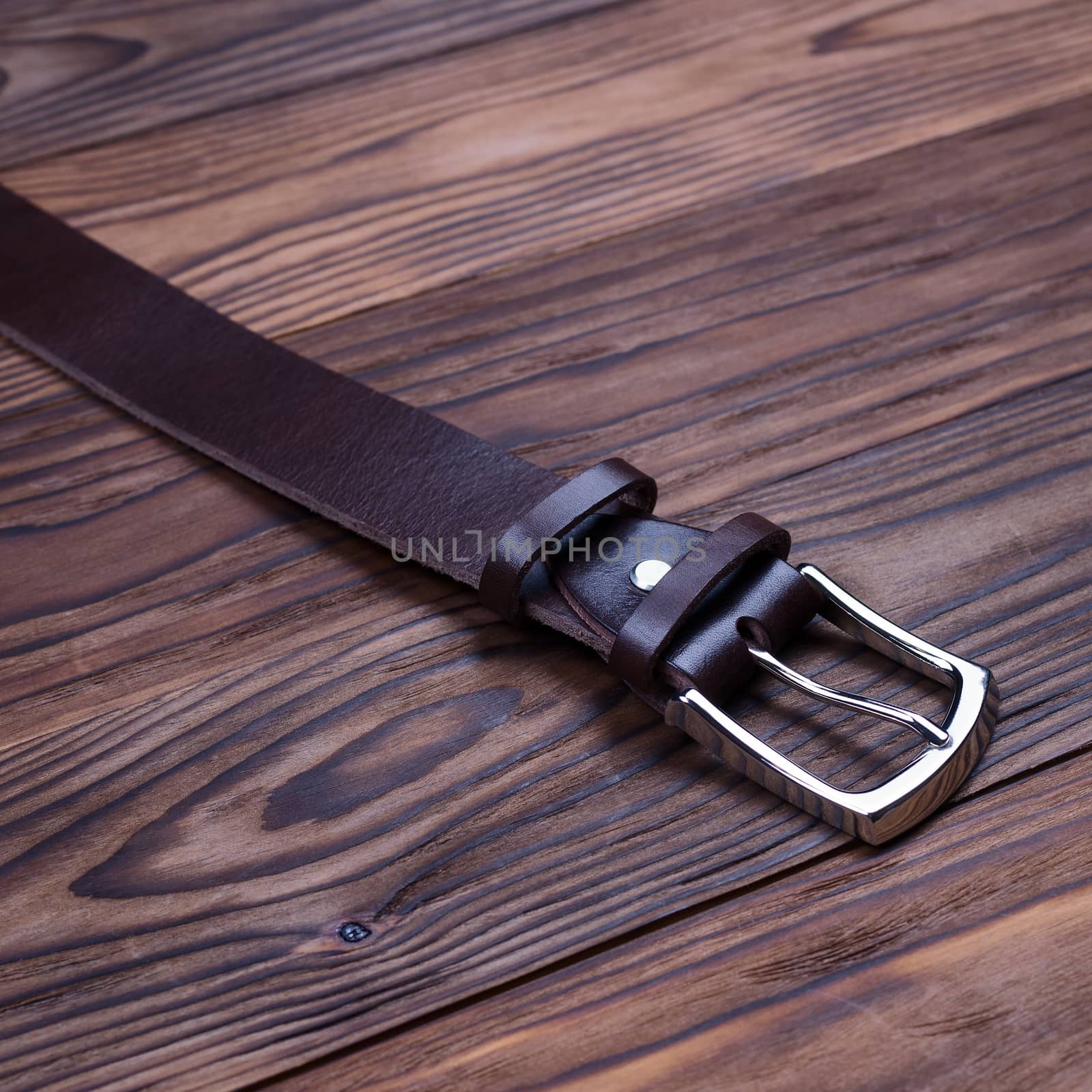 Brown handmade belt buckle lies on textured wooden background closeup. Side view. Stock photo of businessman accessories. by alexsdriver