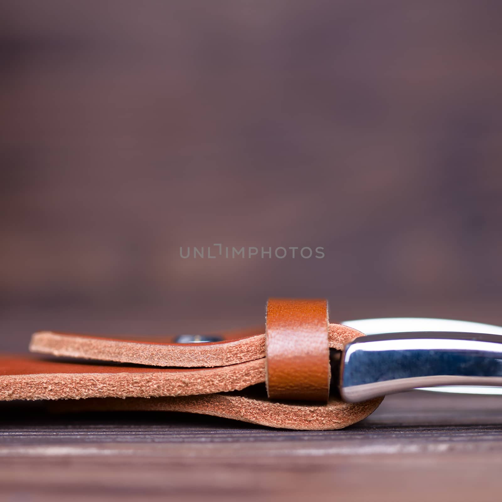 Ginger color handmade belt buckle lies on textured wooden background closeup. Side view. Stock photo of businessman accessories with blurred background.