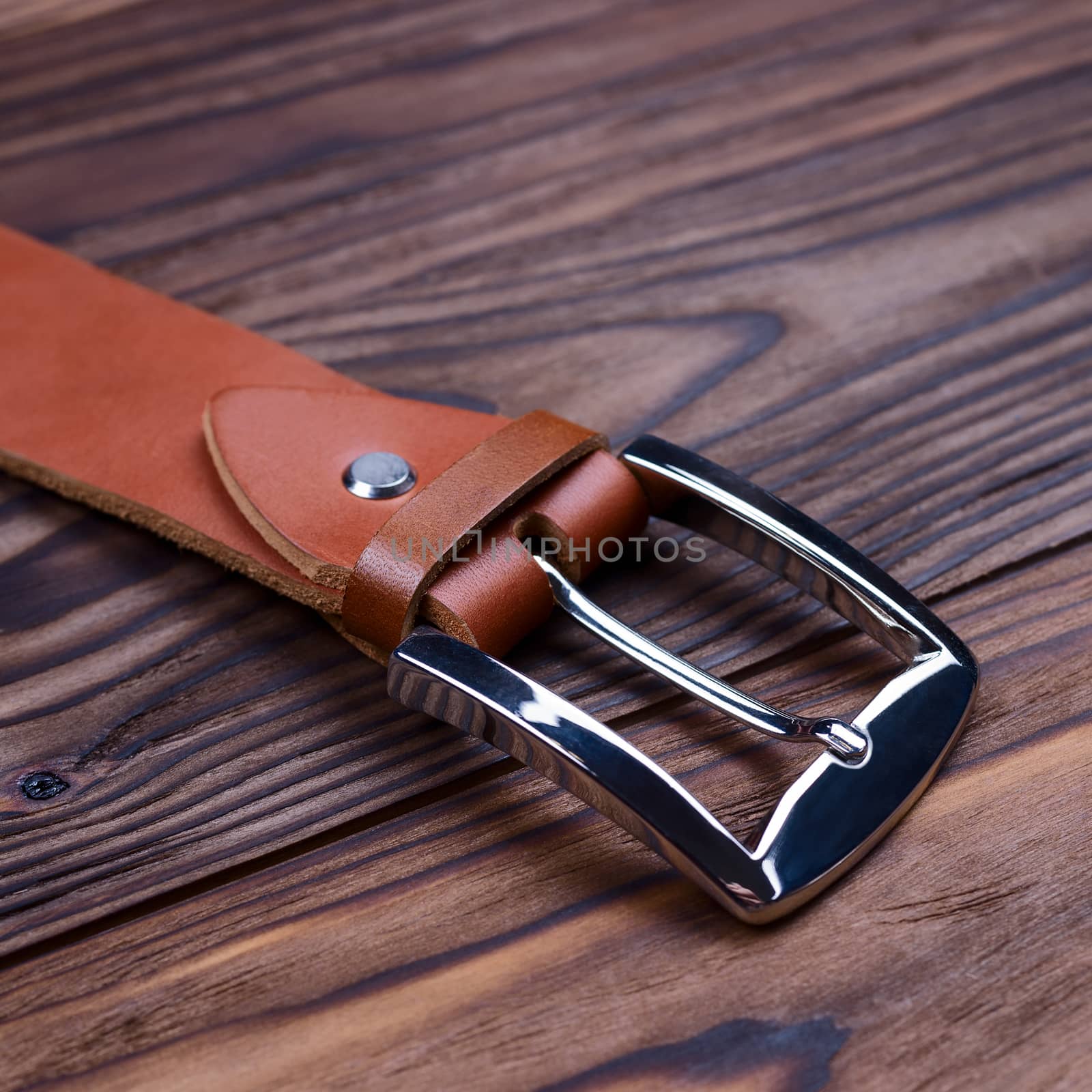 Hue ginger color handmade belt buckle lies on textured wooden background closeup. Side view. Stock photo of businessman accessories.