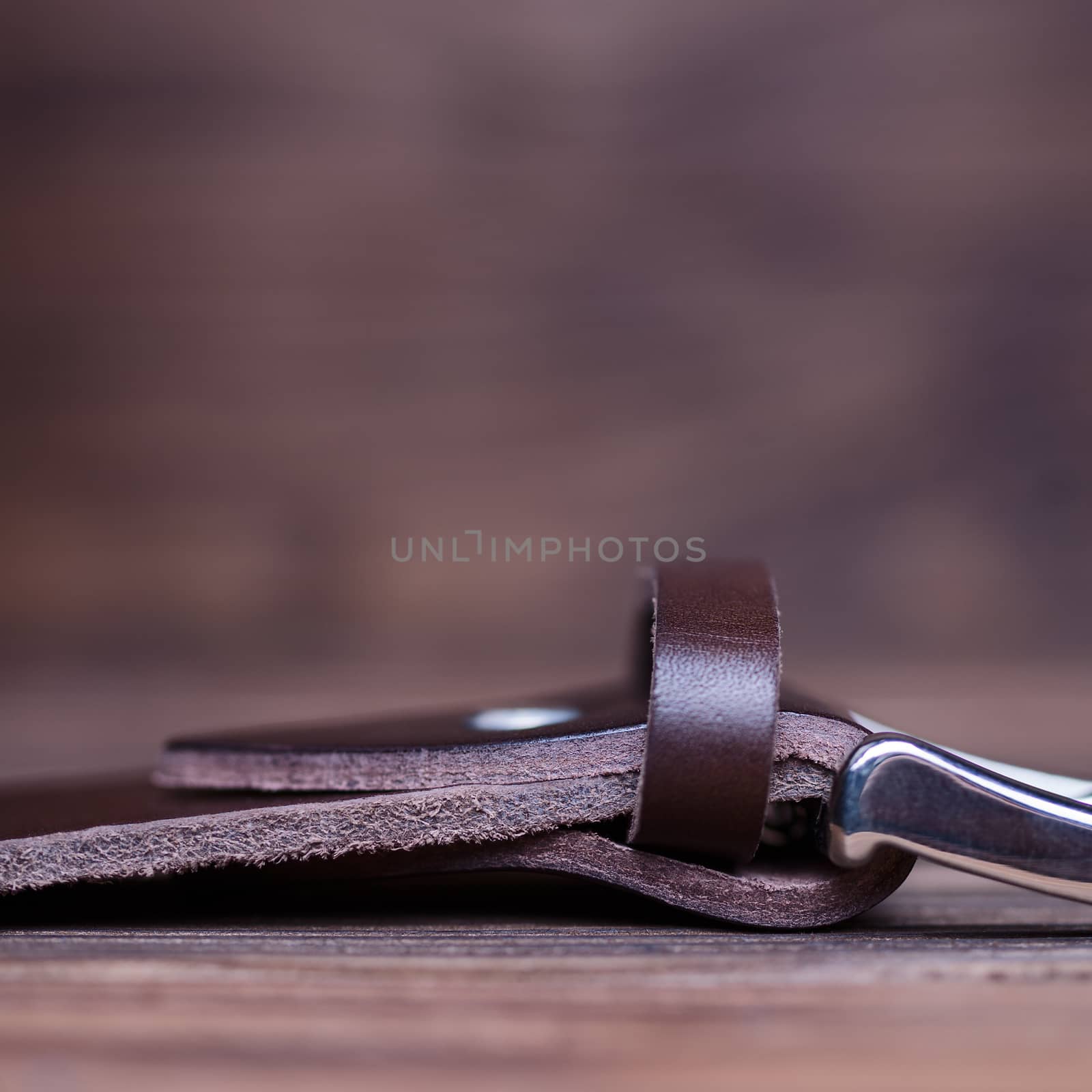 Brown handmade belt buckle lies on textured wooden background closeup. Side view. Stock photo of businessman accessories with blurred background.