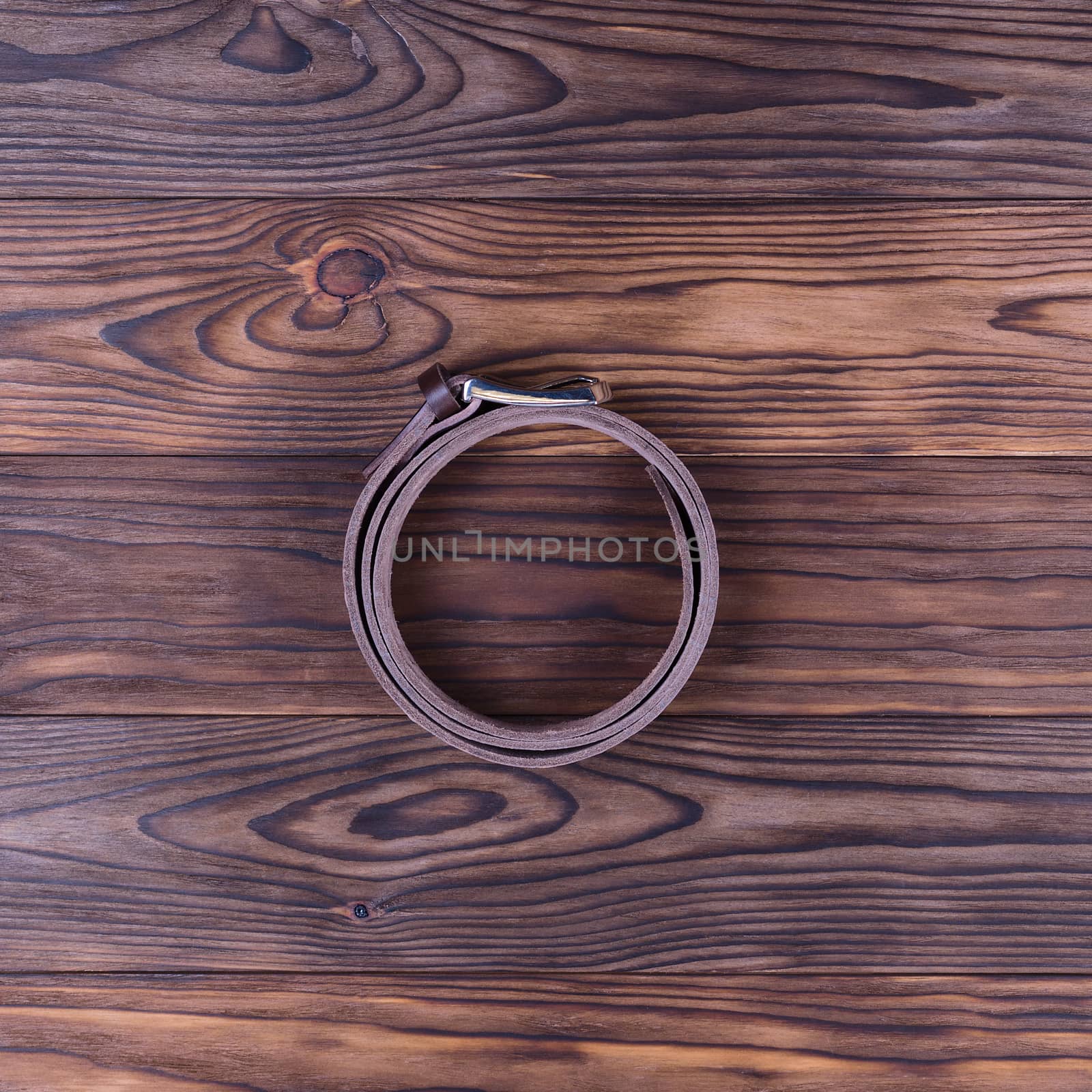 Brown color handmade belt lies on textured wooden background. The belt is twisted into a ring. Up to down view. Stock photo of businessman accessories.