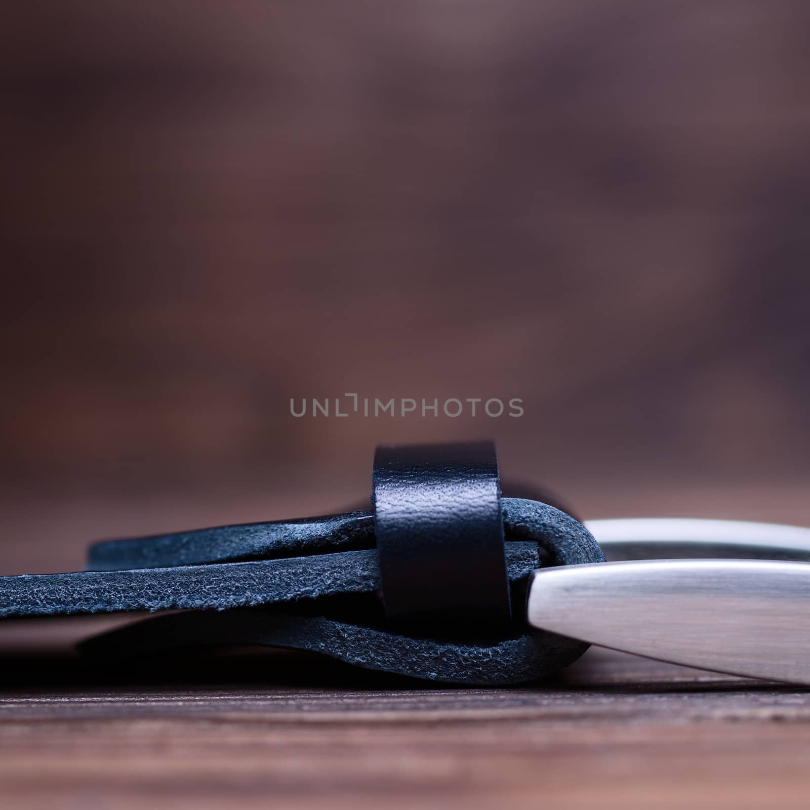 Black handmade belt buckle lies on textured wooden background closeup. Side view. Stock photo of businessman accessories with blurred background.