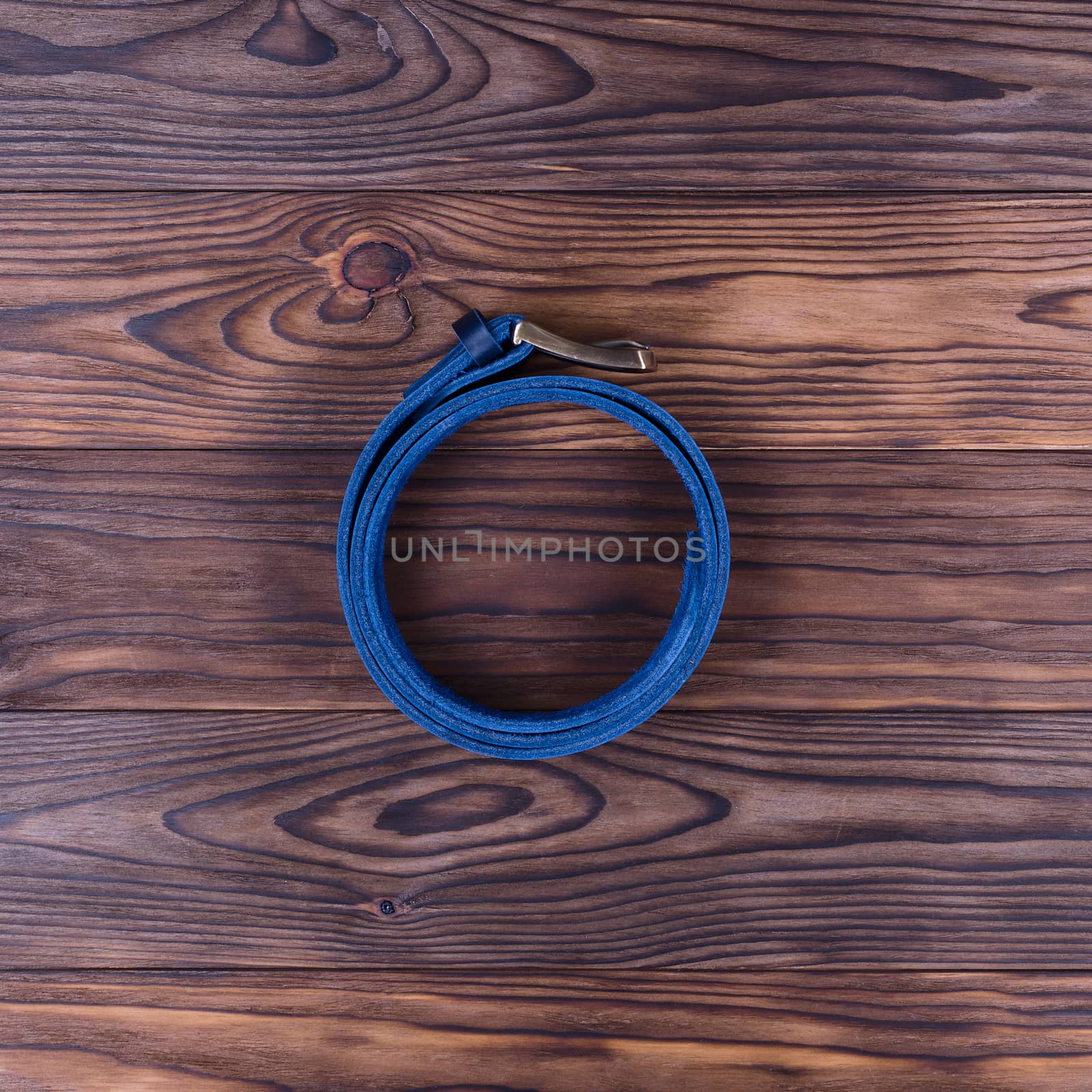 Hue blue color handmade belt lies on textured wooden background. The belt is twisted into a ring. Up to down view. Stock photo of businessman accessories.