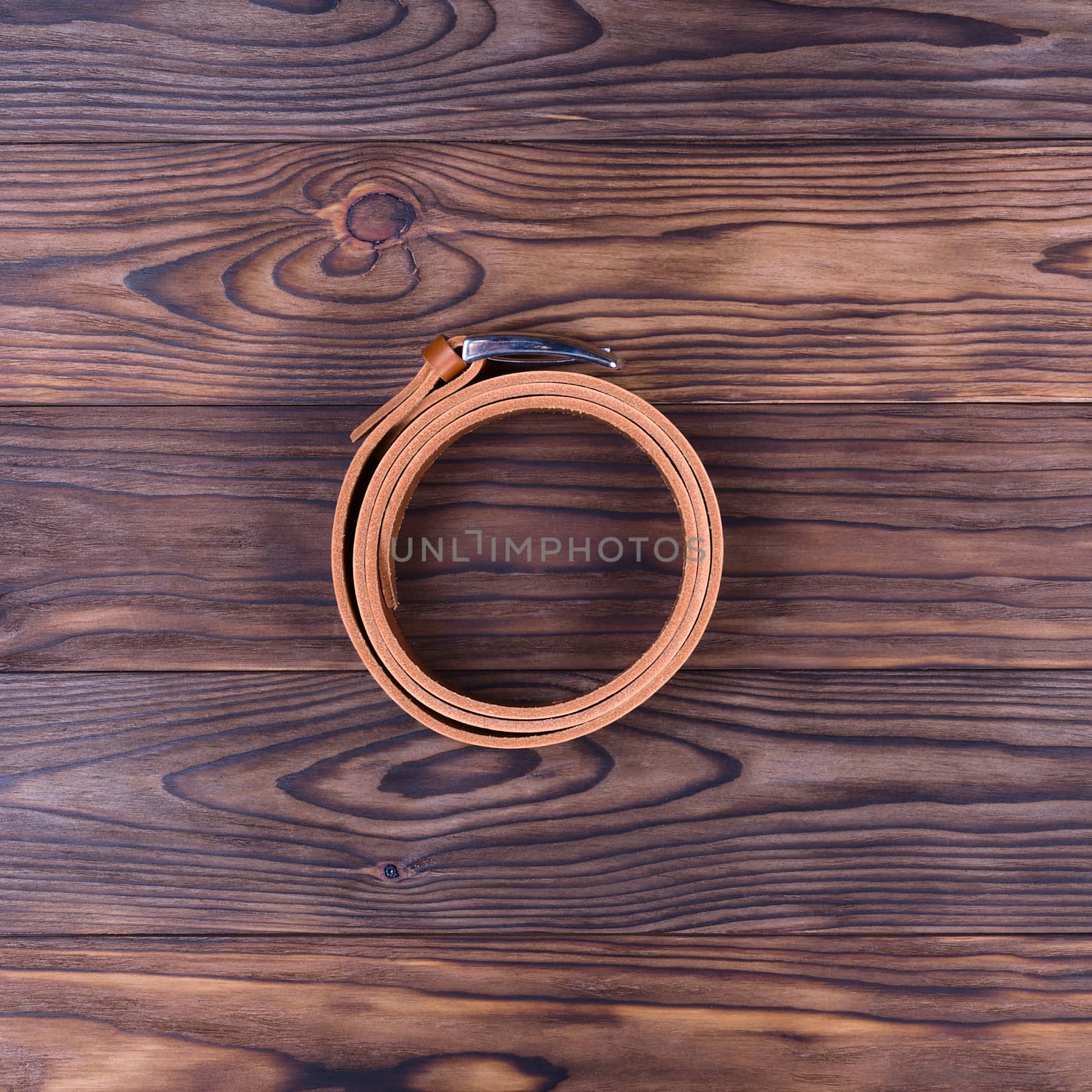 Hue ginger color handmade belt lies on textured wooden background. The belt is twisted into a ring. Up to down view. Stock photo of businessman accessories.
