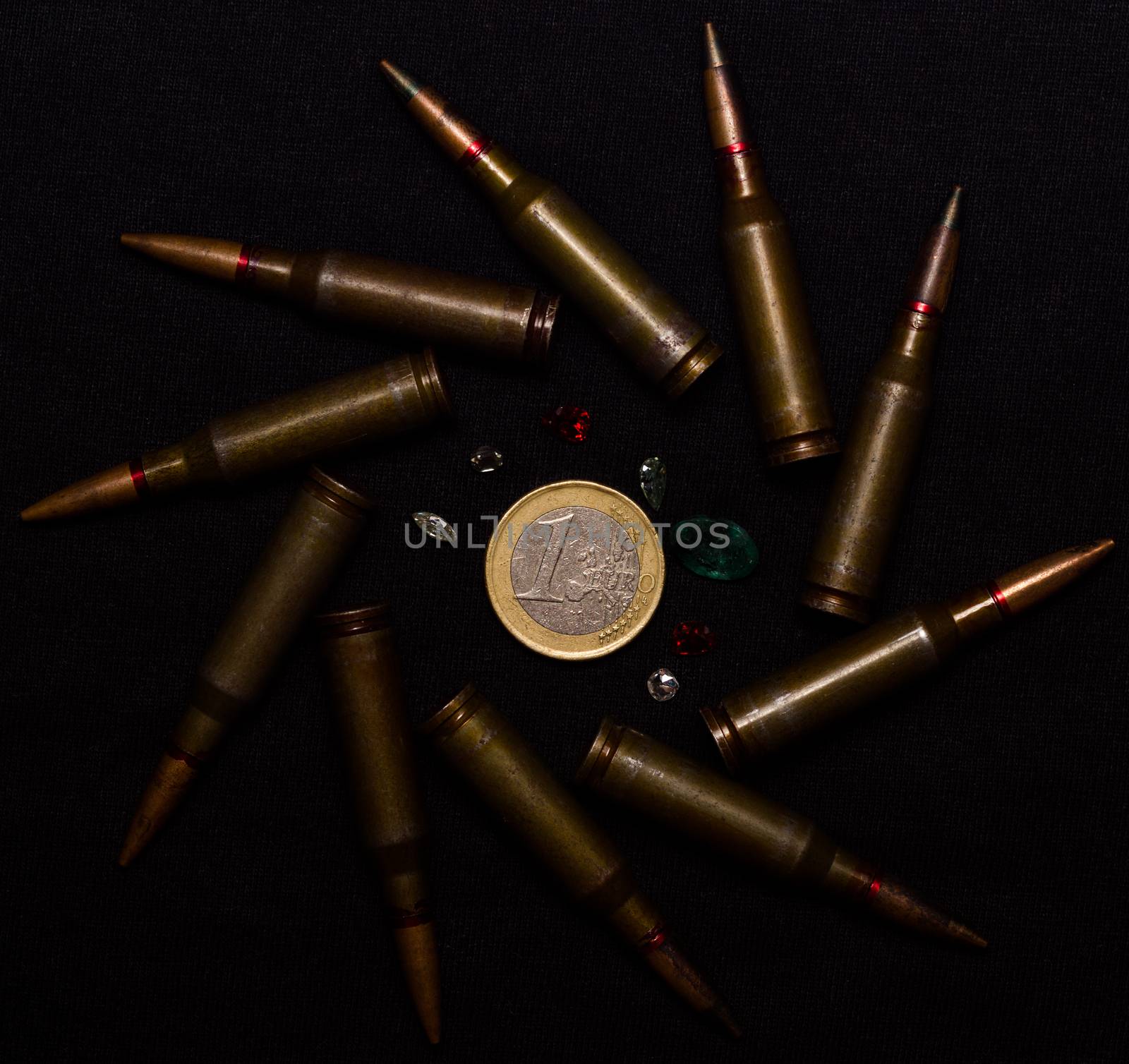 Rifle ammo with a lot of gemstones around one euro coin on black background. Symbolizes the war for money and one of the world's problems.