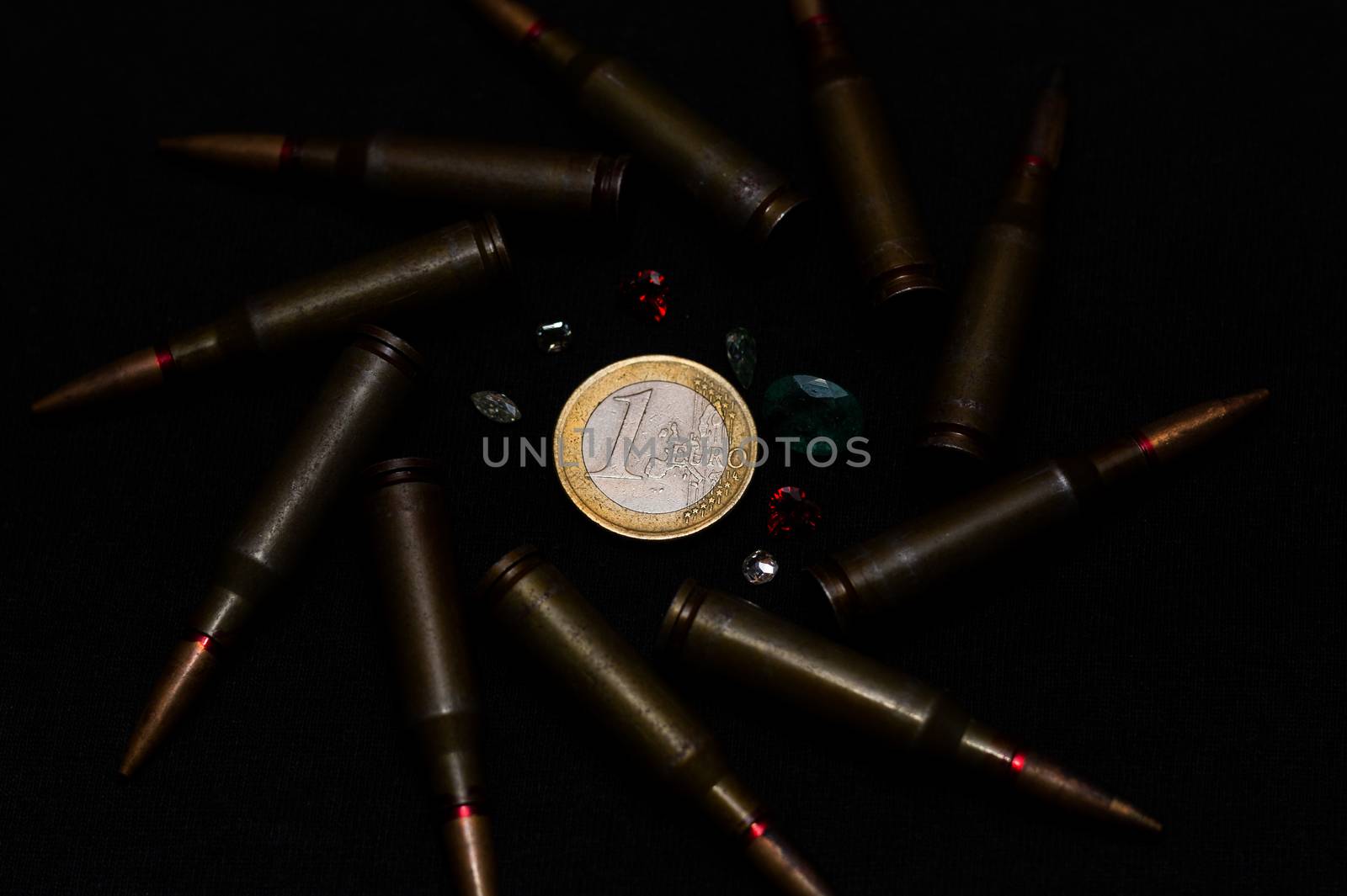 Rifle ammo with a lot of gemstones around one euro coin on black background. Symbolizes the war for money and one of the world's problems.