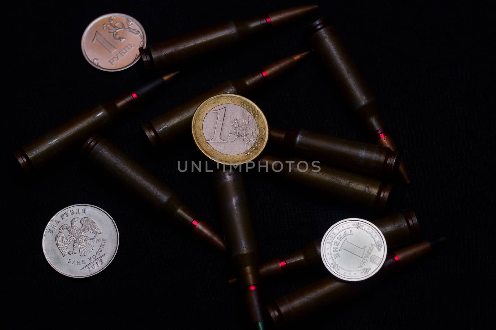 One euro, one Russian ruble and Ukrainian hryvna coins with rifle military ammo on black background. Symbolizes war for money- biggest problem in world.