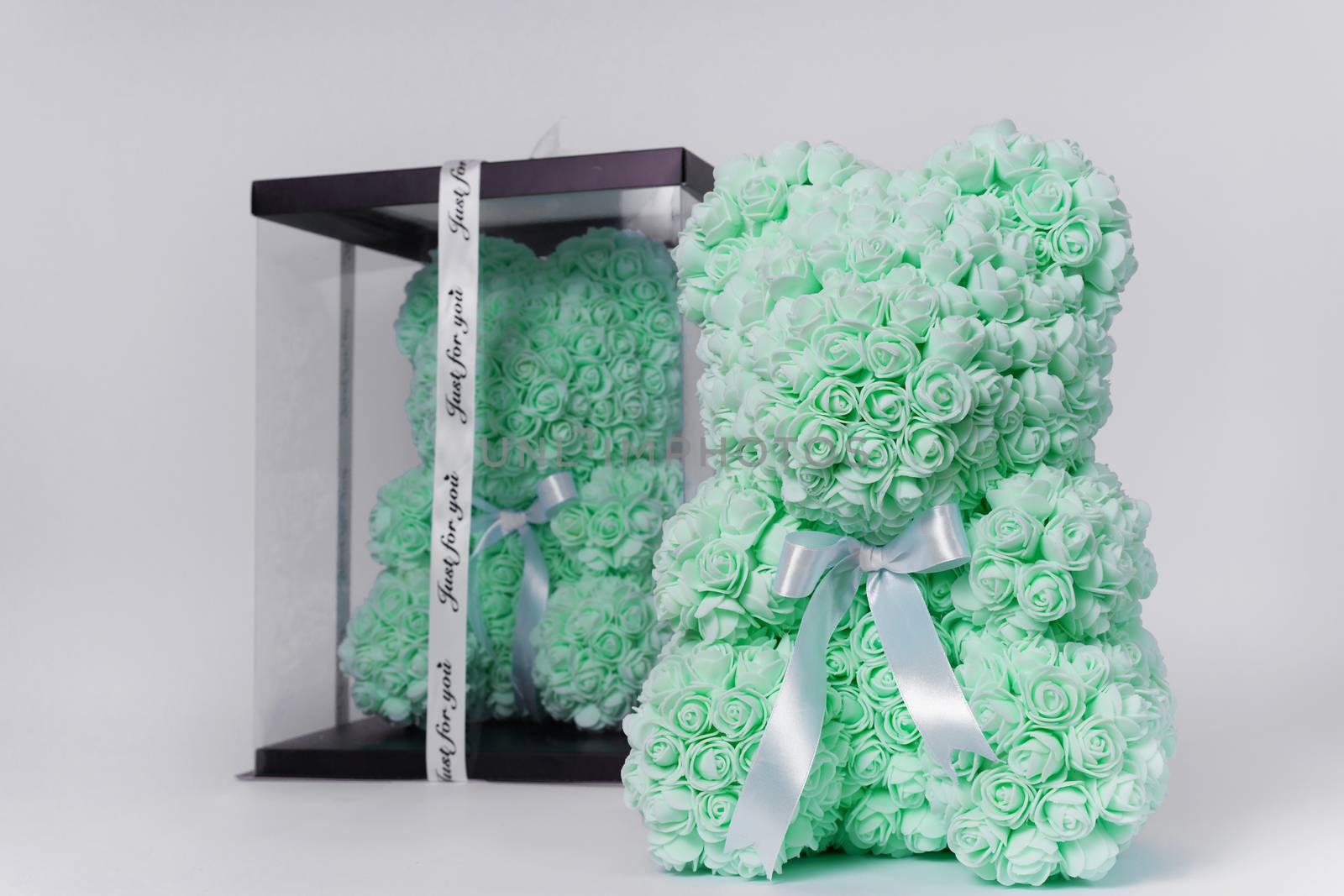Green teddy bear toy of foamirane roses. The same teddy in clear box with black paper cover on background. White stripe on teddy neck. Stock photo isolated on white background. Gift on holiday for women.