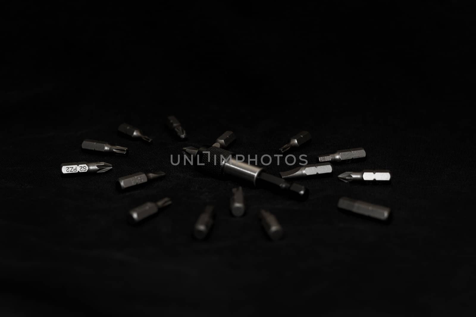 Tool carbon steel bits on black background in dark key style. Bit holder in center and bits around bit holder.