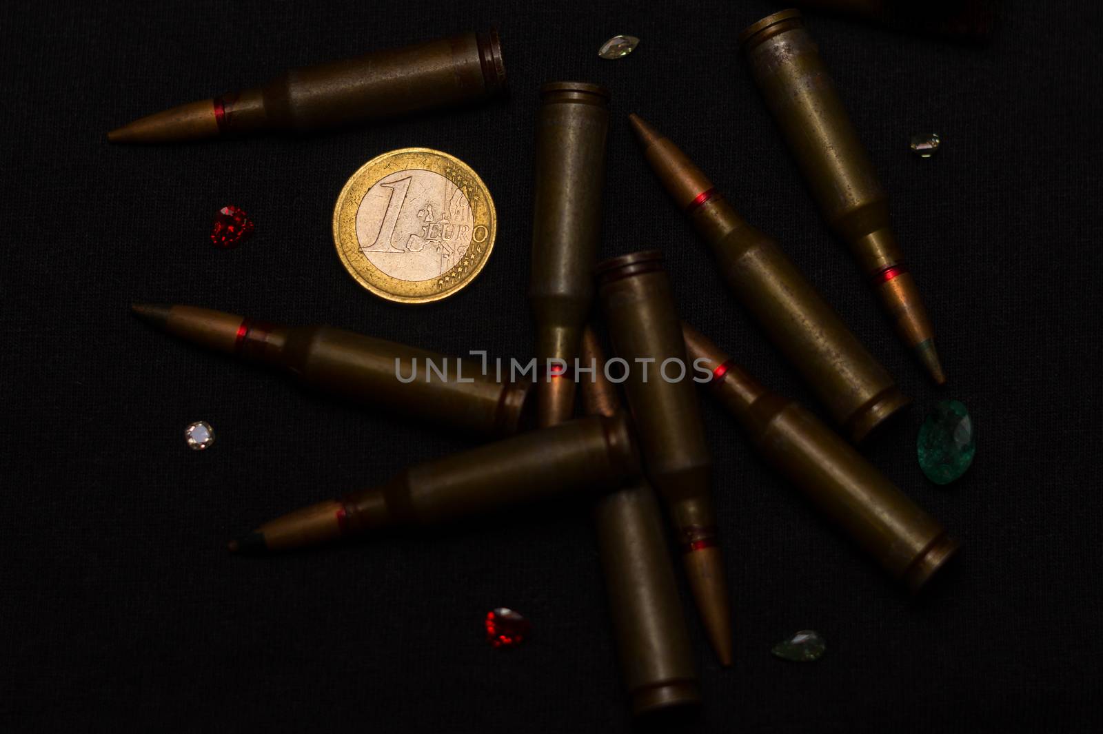 Rifle ammo around one euro coin wigh gemstones on black background. Symbolizes the war for money and one of the world's problems. by alexsdriver