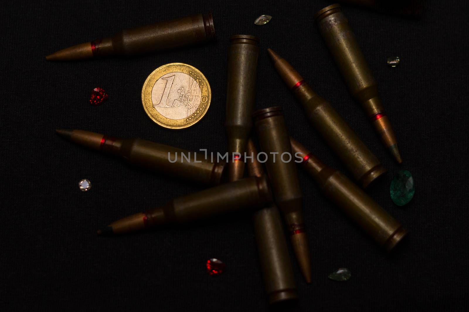 Rifle ammo around one euro coin wigh gemstones on black background. Symbolizes the war for money and one of the world's problems.