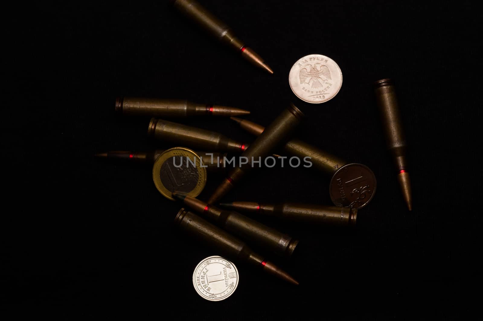 One euro, one Russian ruble and Ukrainian hryvna coins with rifle military ammo on black background. Symbolizes war for money- biggest problem in world.