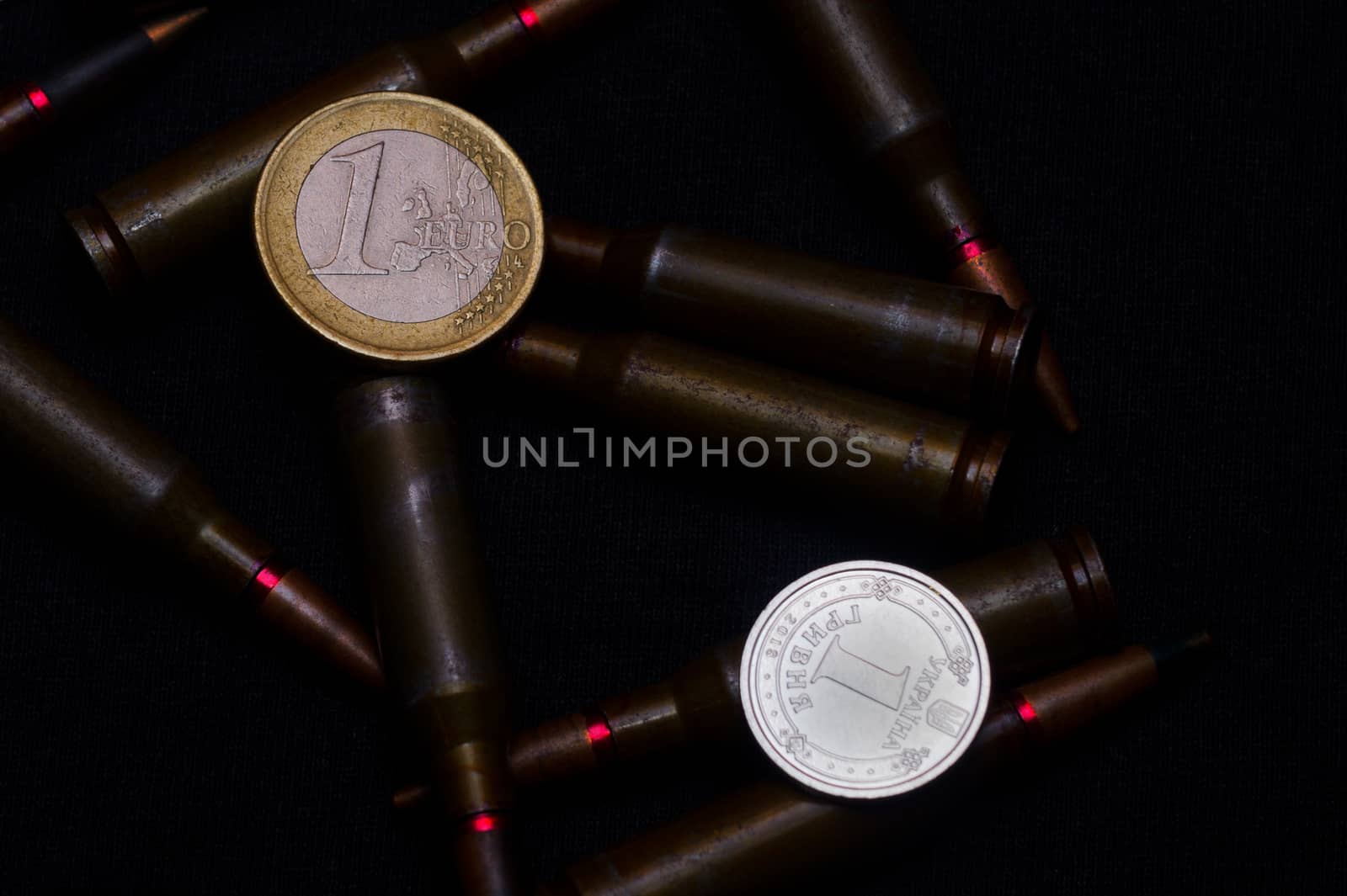 One euro and Ukrainian hryvna coins with rifle military ammo on black background. Symbolizes war for money- biggest problem in world.