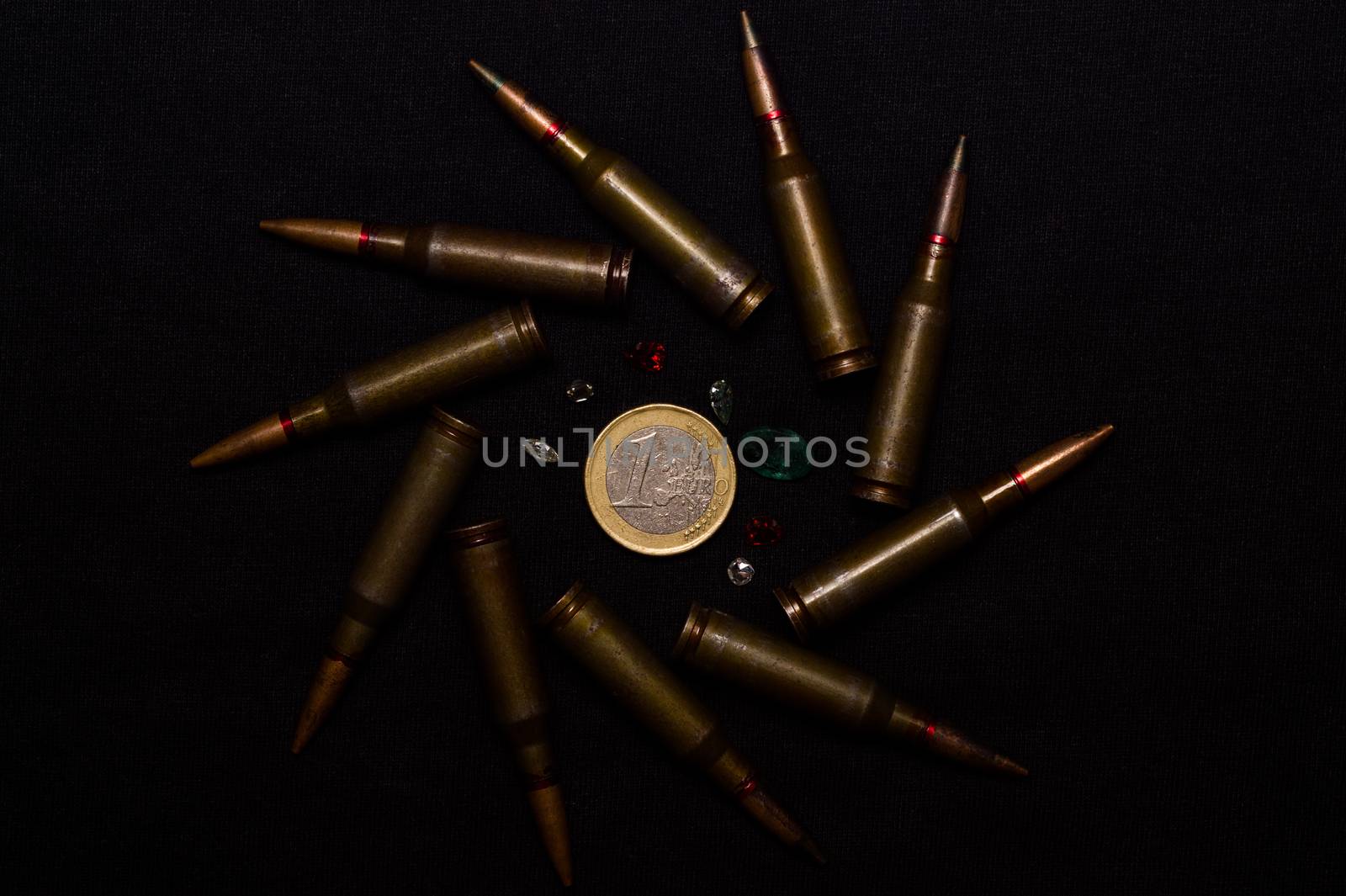 Rifle ammo with a lot of gemstones around one euro coin on black background. Symbolizes the war for money and one of the world's problems.